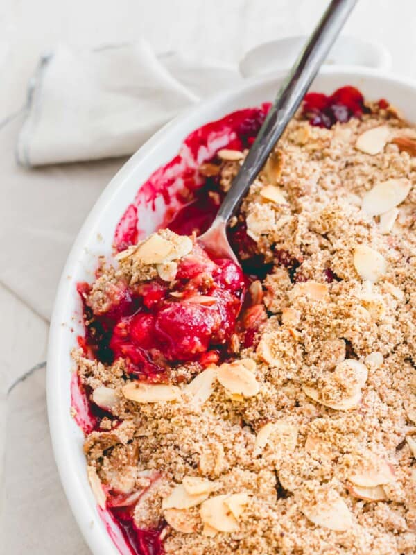 Sour cherry crisp in a white baking dish with a spoon.