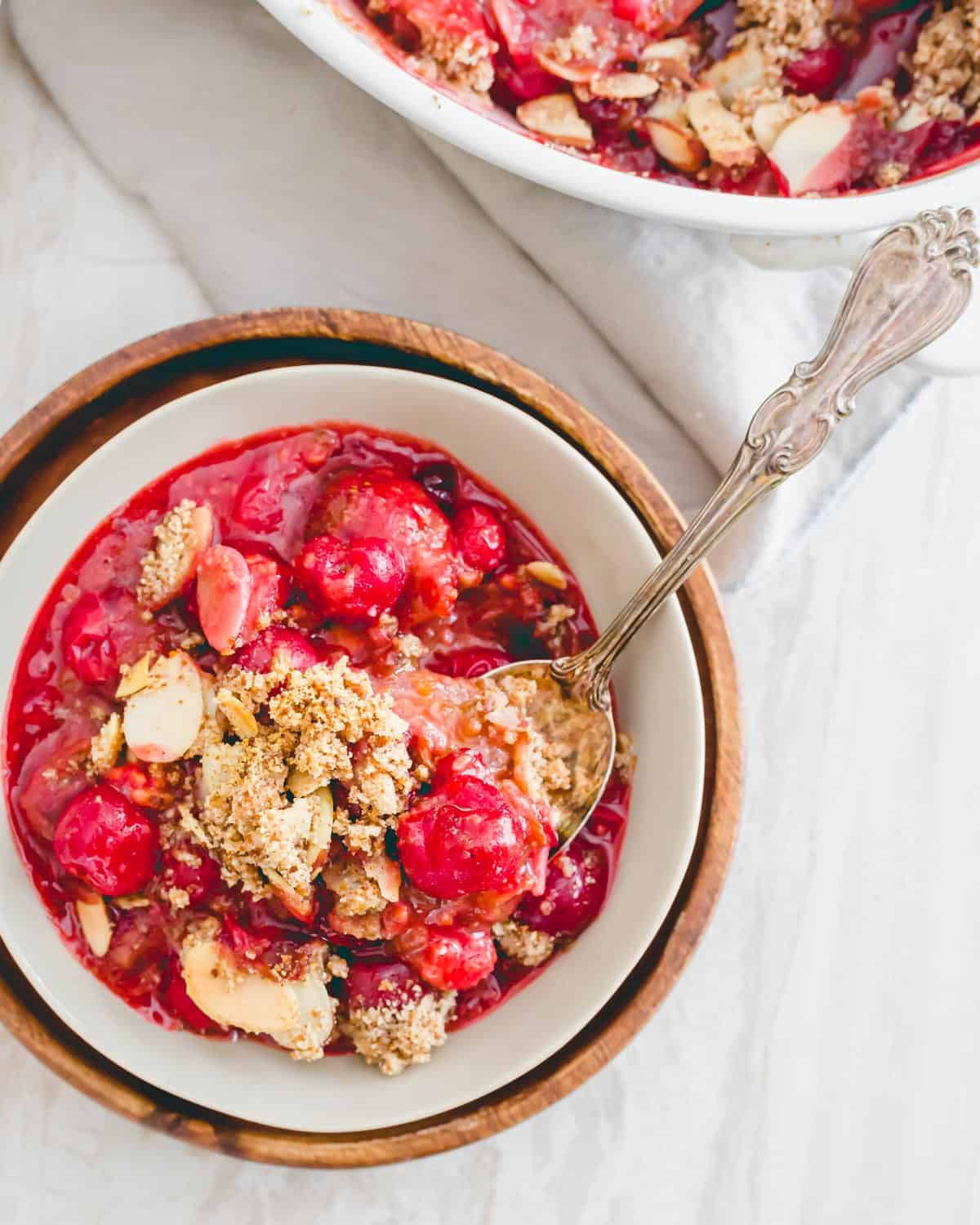 Tart cherry crumble in a serving bowl with a spoon.