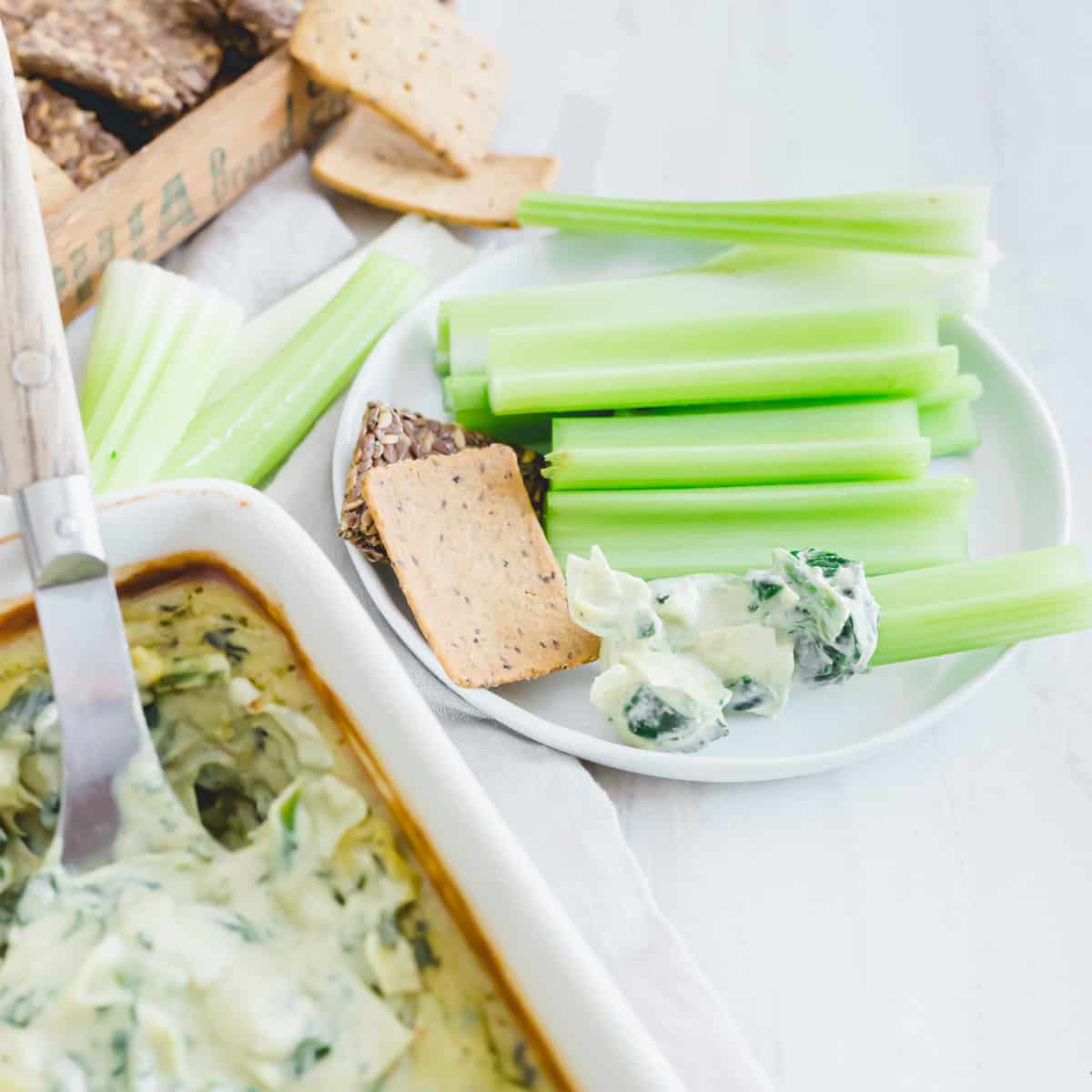 Plate of celery sticks and crackers with vegan spinach and artichoke dip.