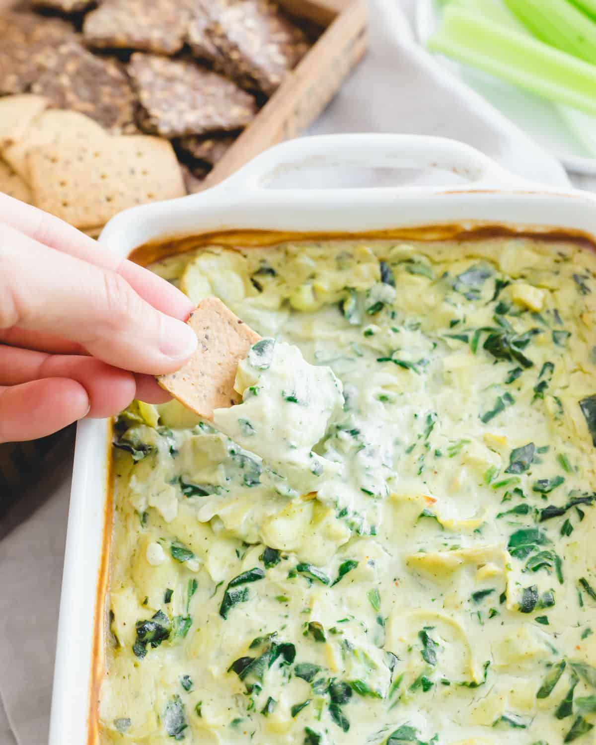 Vegan spinach artichoke dip in a baking dish with crackers.