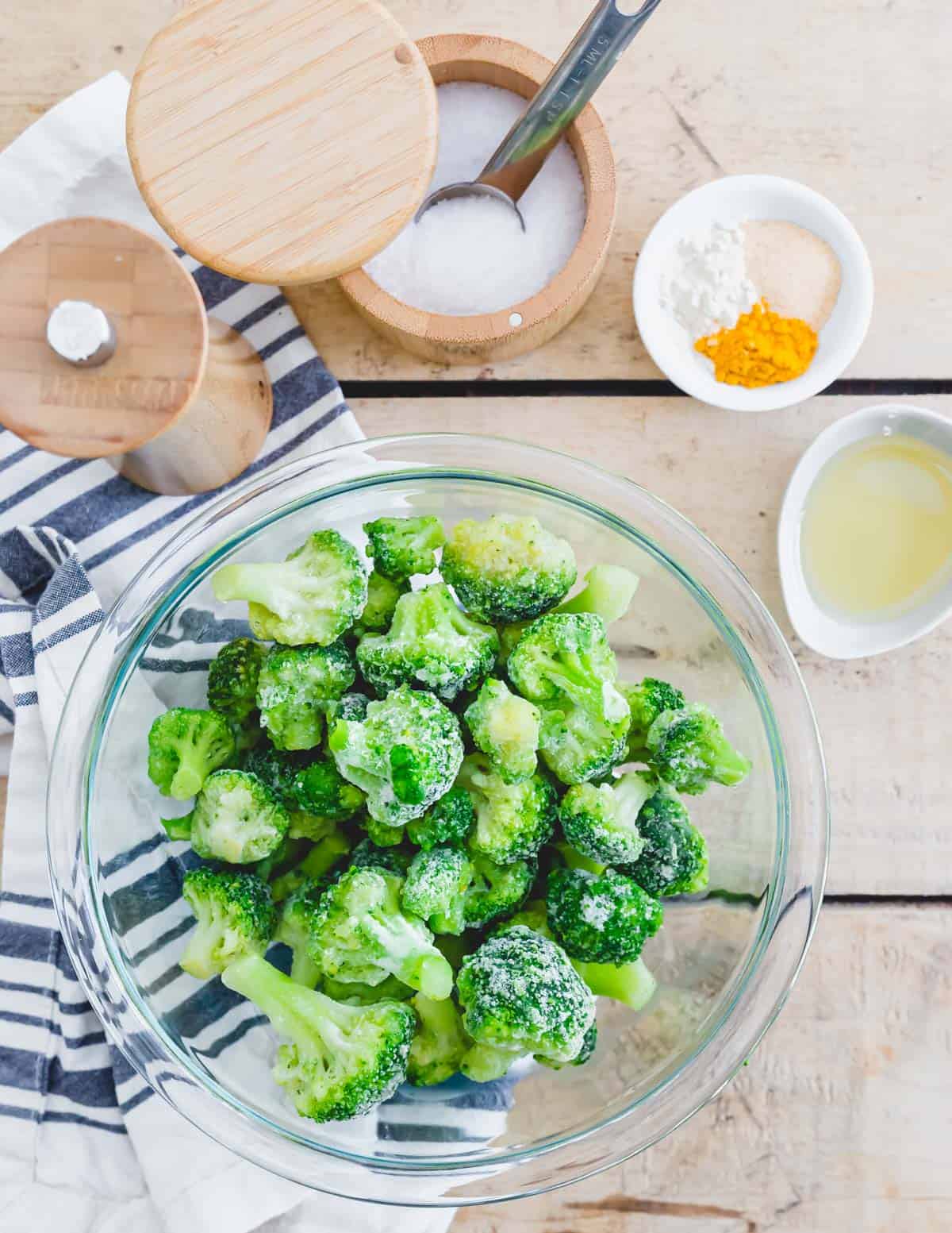 Frozen broccoli in a bowl with spices, avocado oil, salt and pepper.