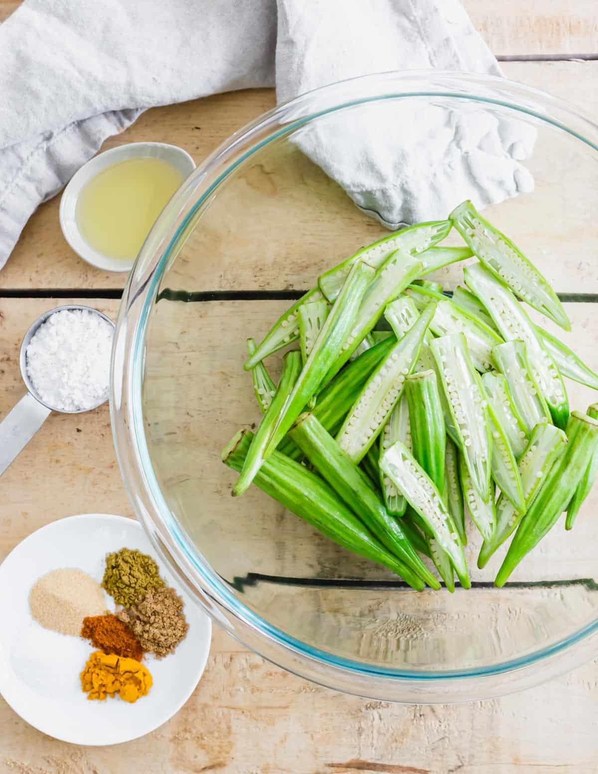 Okra sliced in half in a bowl with avocado oil, seasonings and arrowroot powder.