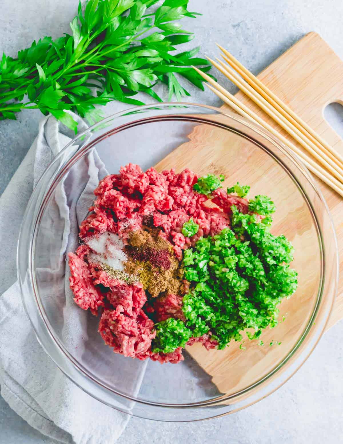 Ground beef in a mixing bowl with parsley, onion and garlic mince and spices to make beef kafta kabobs.