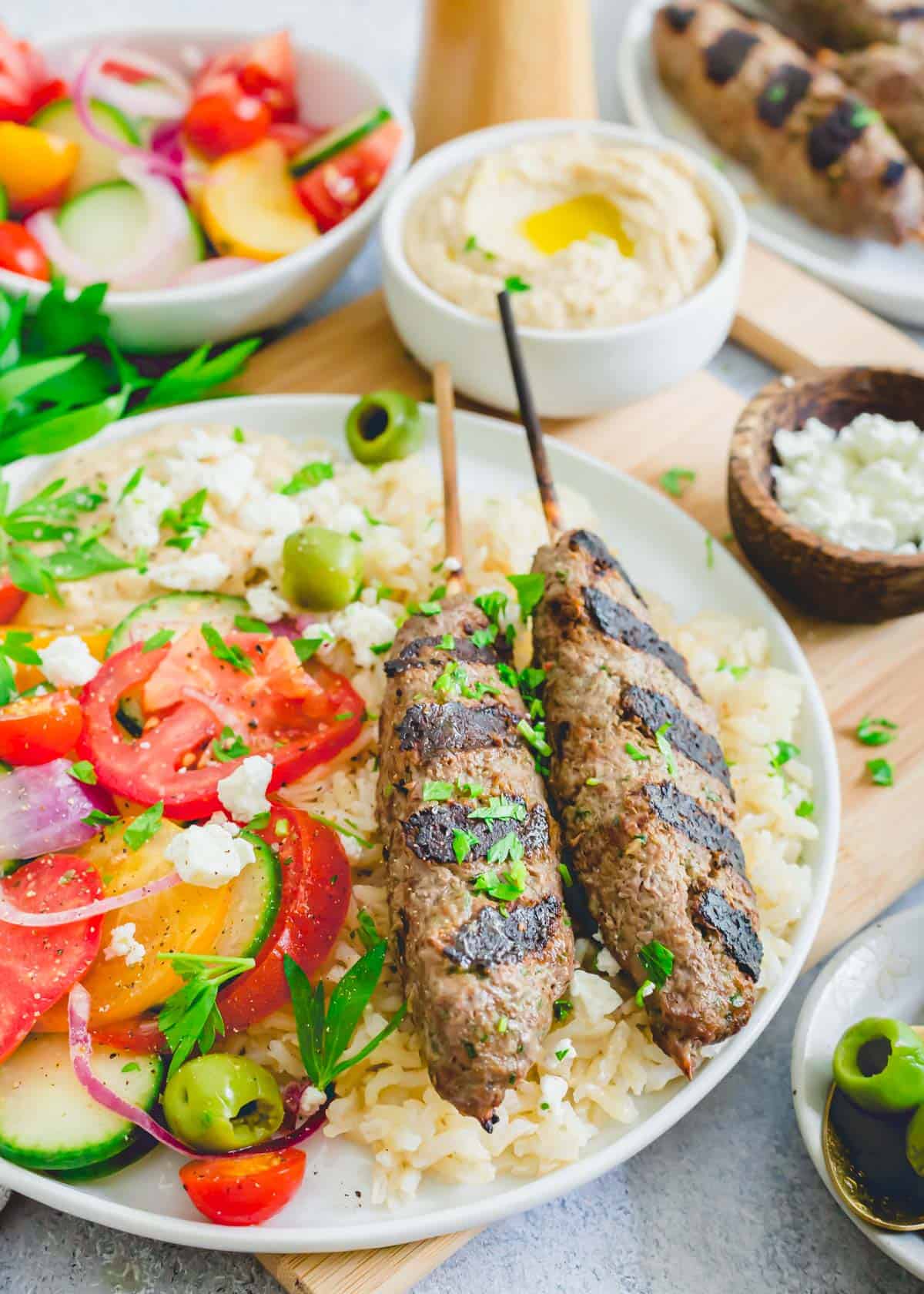 Beef kafta recipe served on kabobs with rice, tomato cucumber salad, hummus and feta.