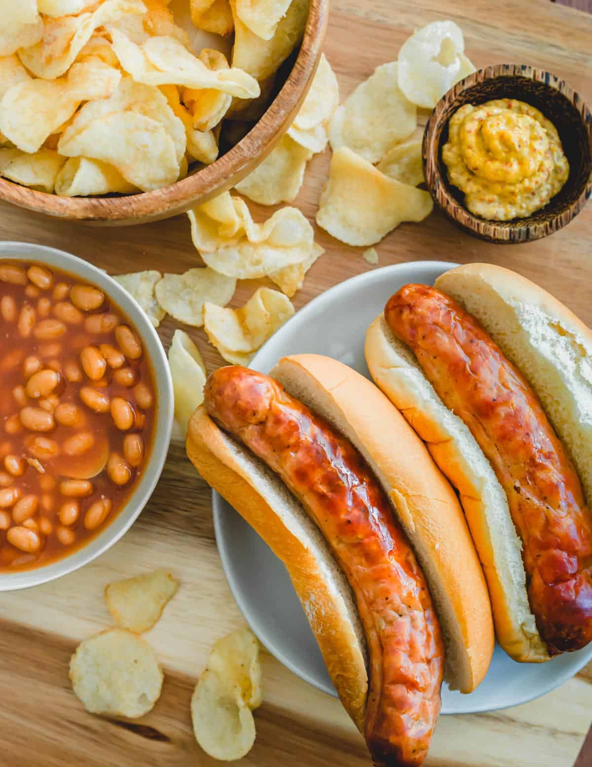 Brats cooked in the air fryer in buns with baked beans and potato chips.