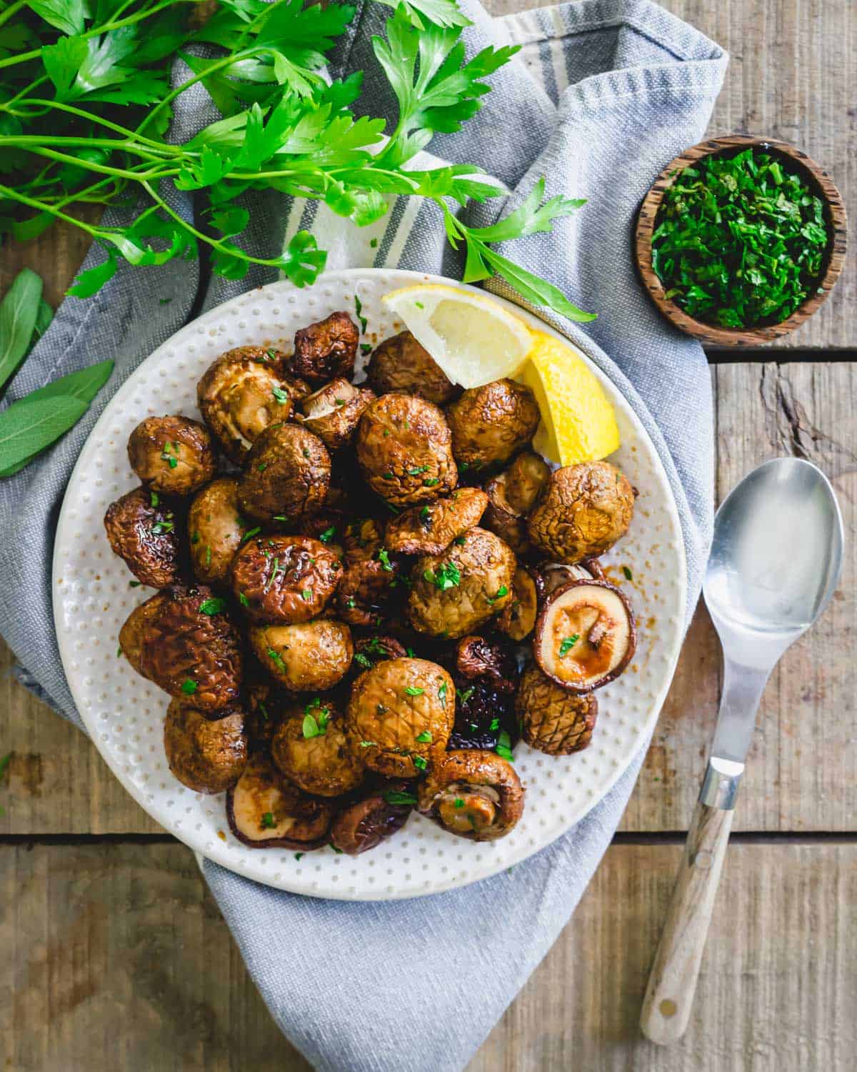 Garlic soy mushrooms cooked in the air fryer on a serving plate with lemon wedges.