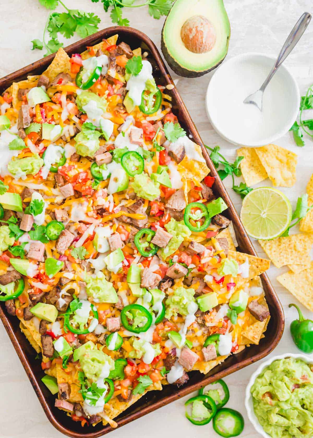 Nachos con carne asada on a baking sheet with lime crema.