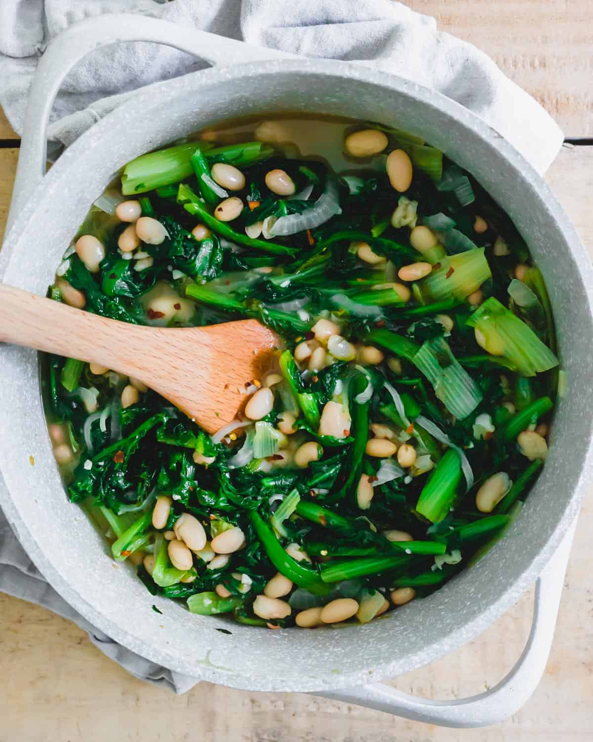 Escarole and beans in a pot with spatula.