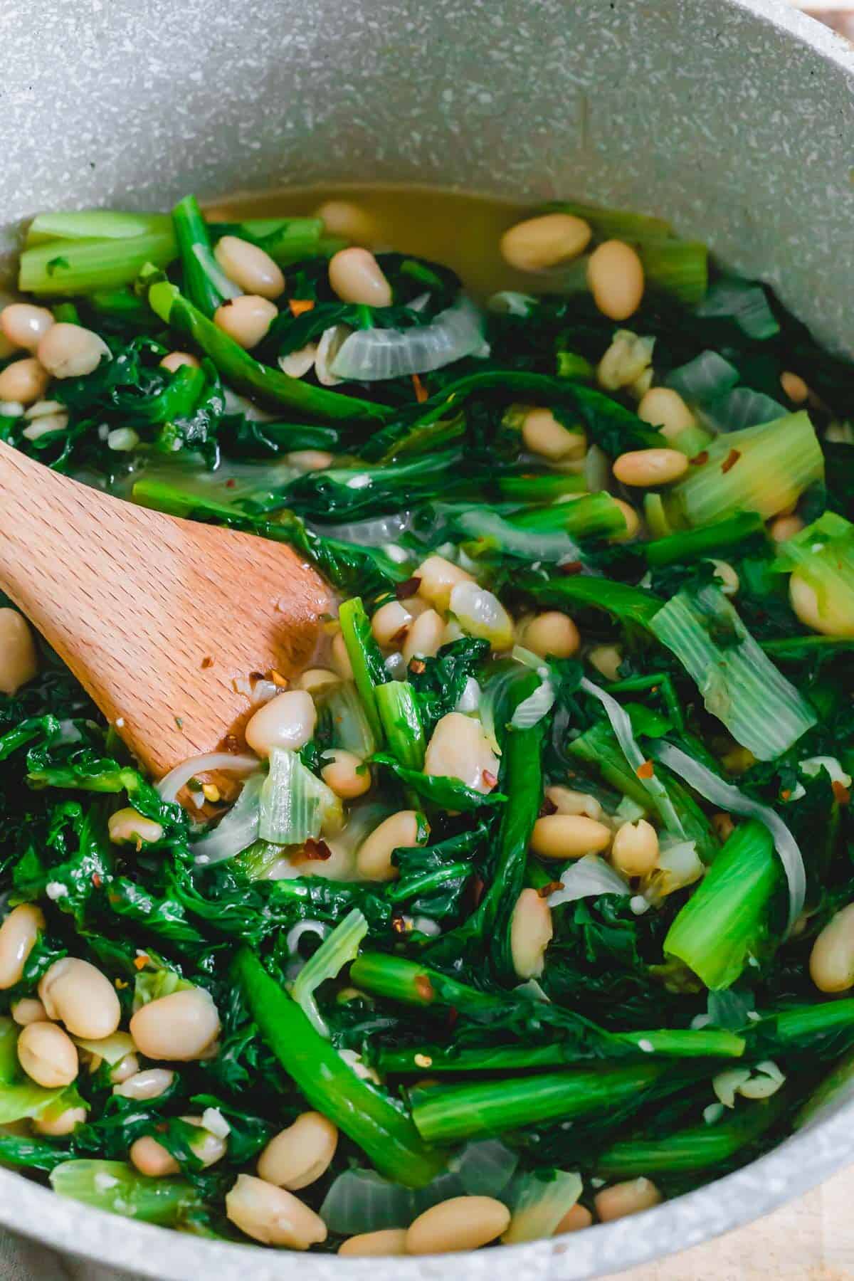 Hearty Italian escarole and beans recipe in a large pot with wooden spatula.