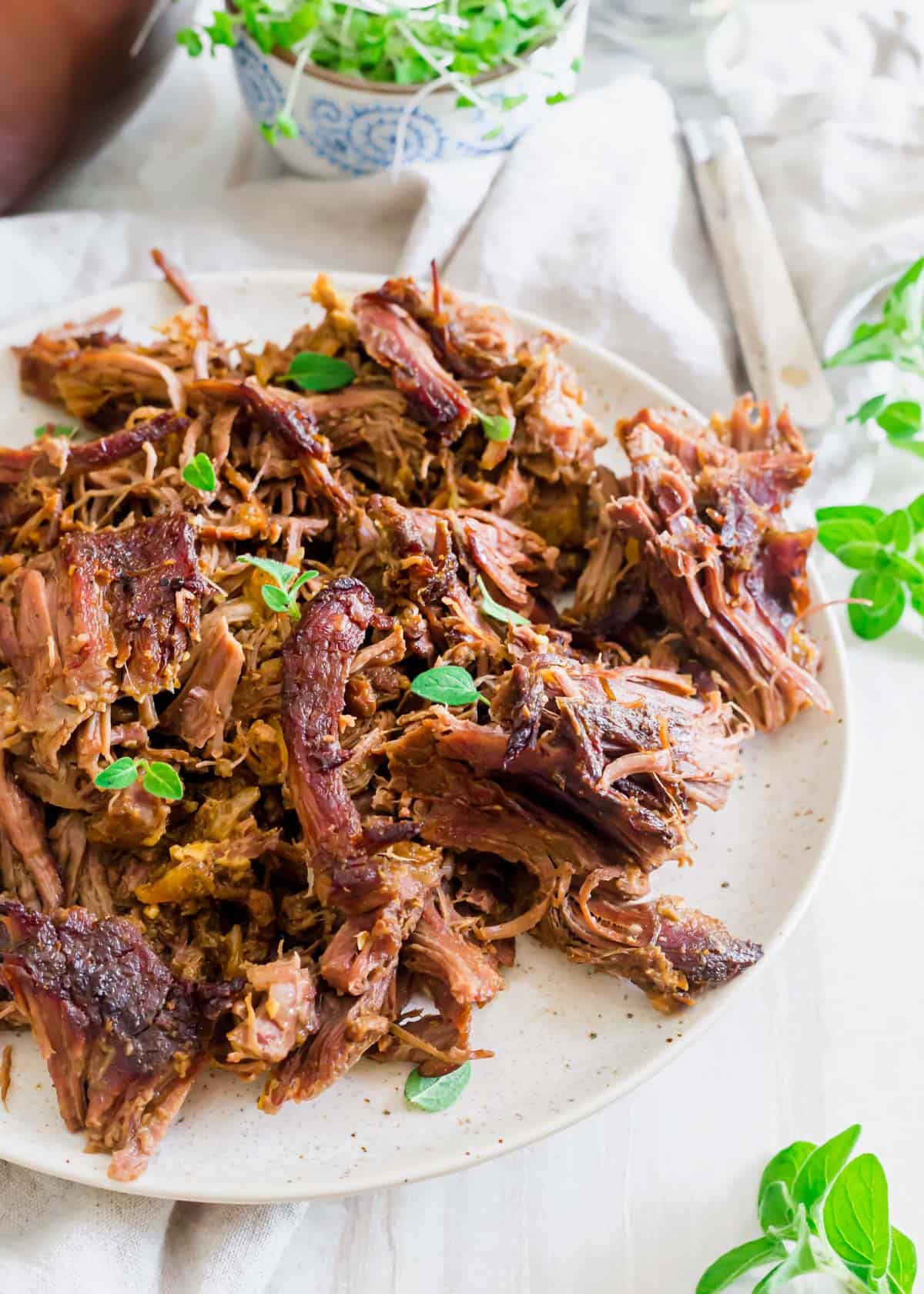 Shredded braised leg of lamb on a plate with fresh oregano can be used in a variety of different lamb dishes.
