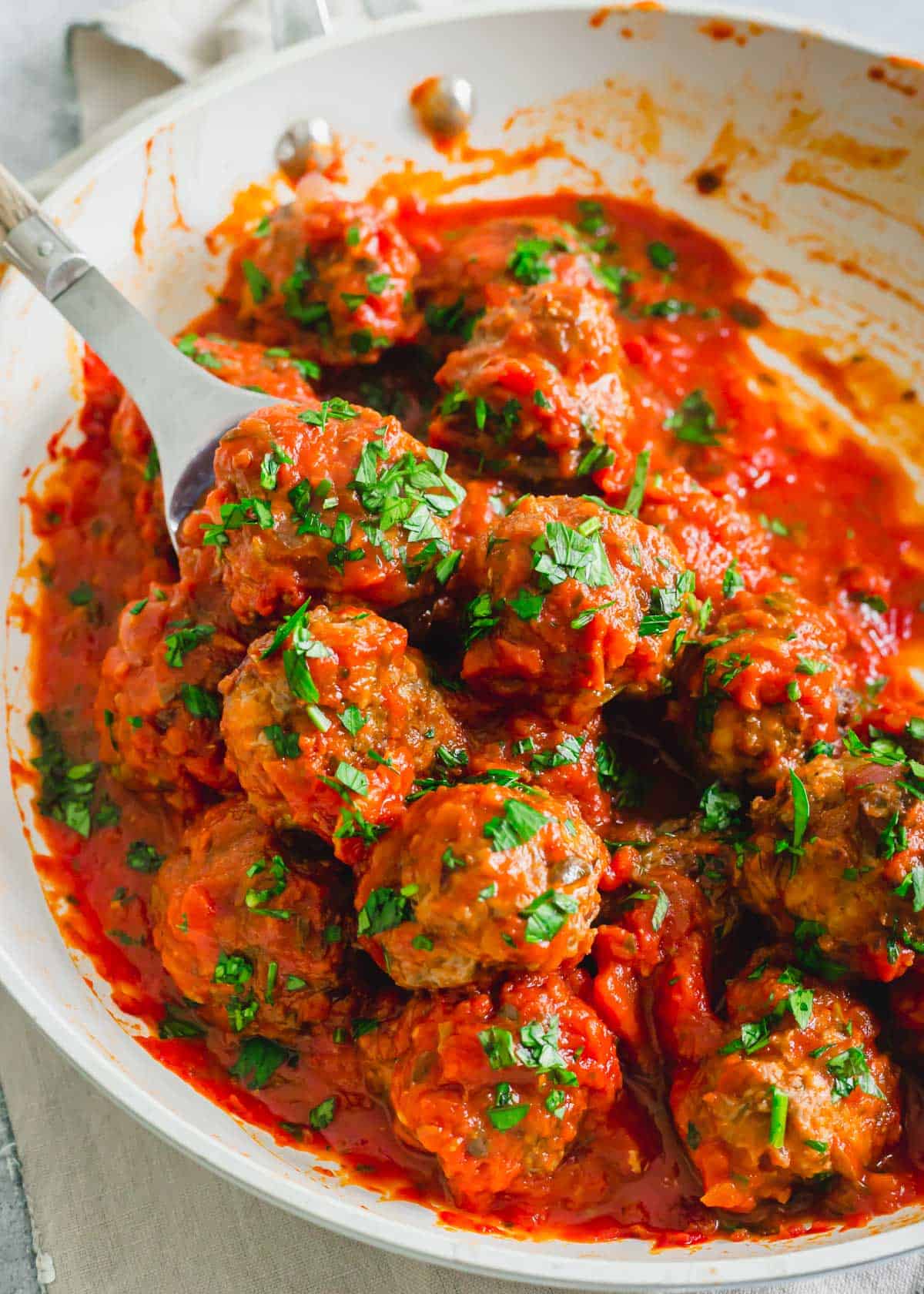 Baked venison meatballs tossed with marinara sauce and fresh parsley in a pan.