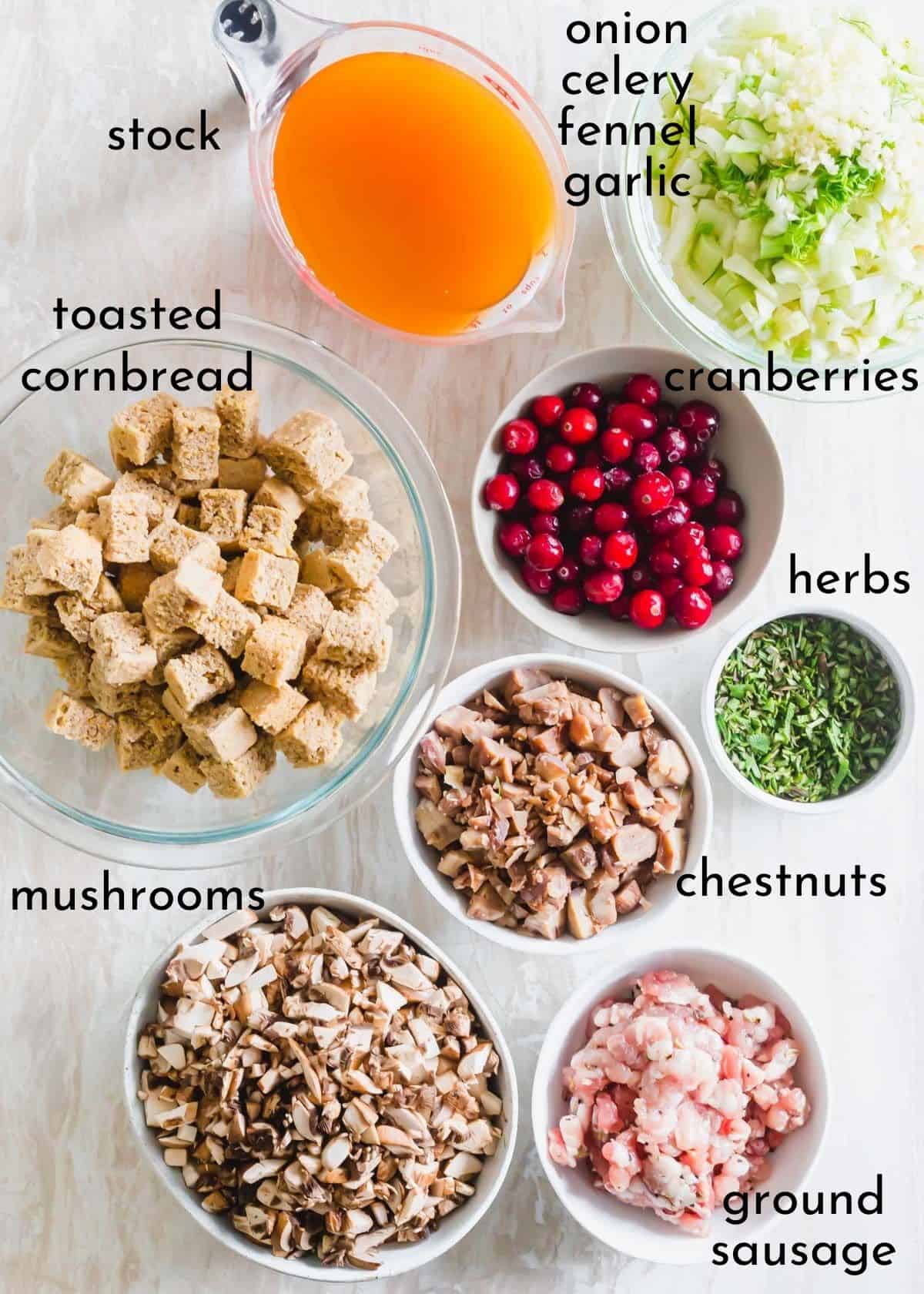 Ingredients to make chestnut stuffing including cornbread, cranberries, sausage, mushrooms, fresh herbs, onion, celery and fennel.