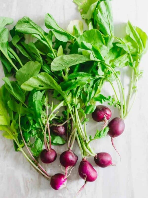 Fresh radishes with green leaves on a light background.