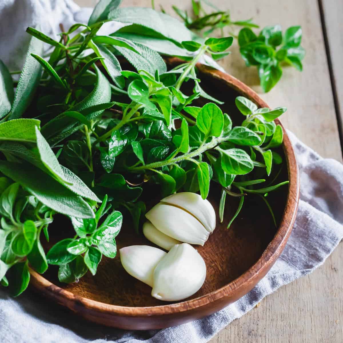 Fresh sage, rosemary, oregano and peeled garlic cloves on a wooden plate.