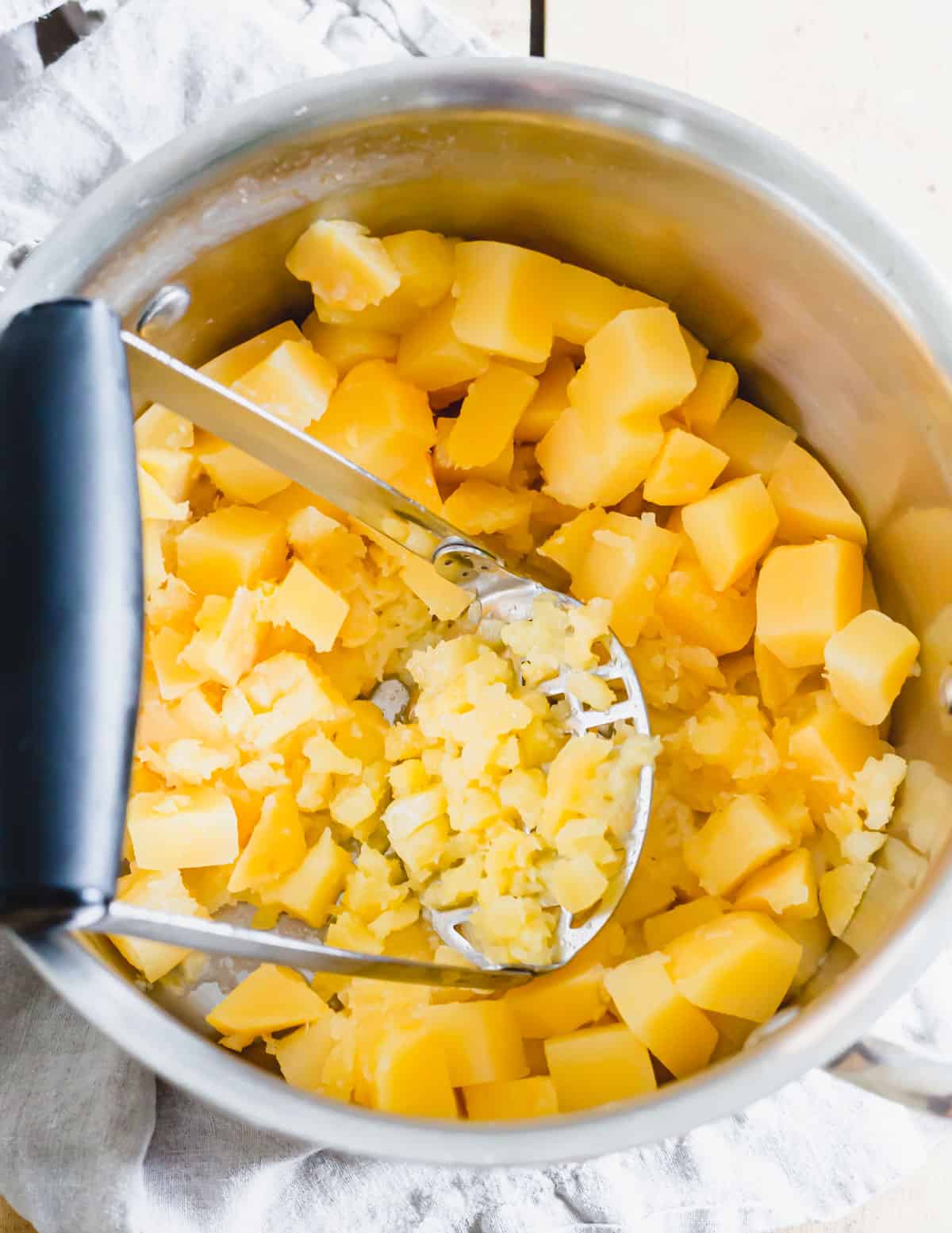 Mashing boiled rutabaga in a pot with a potato masher.