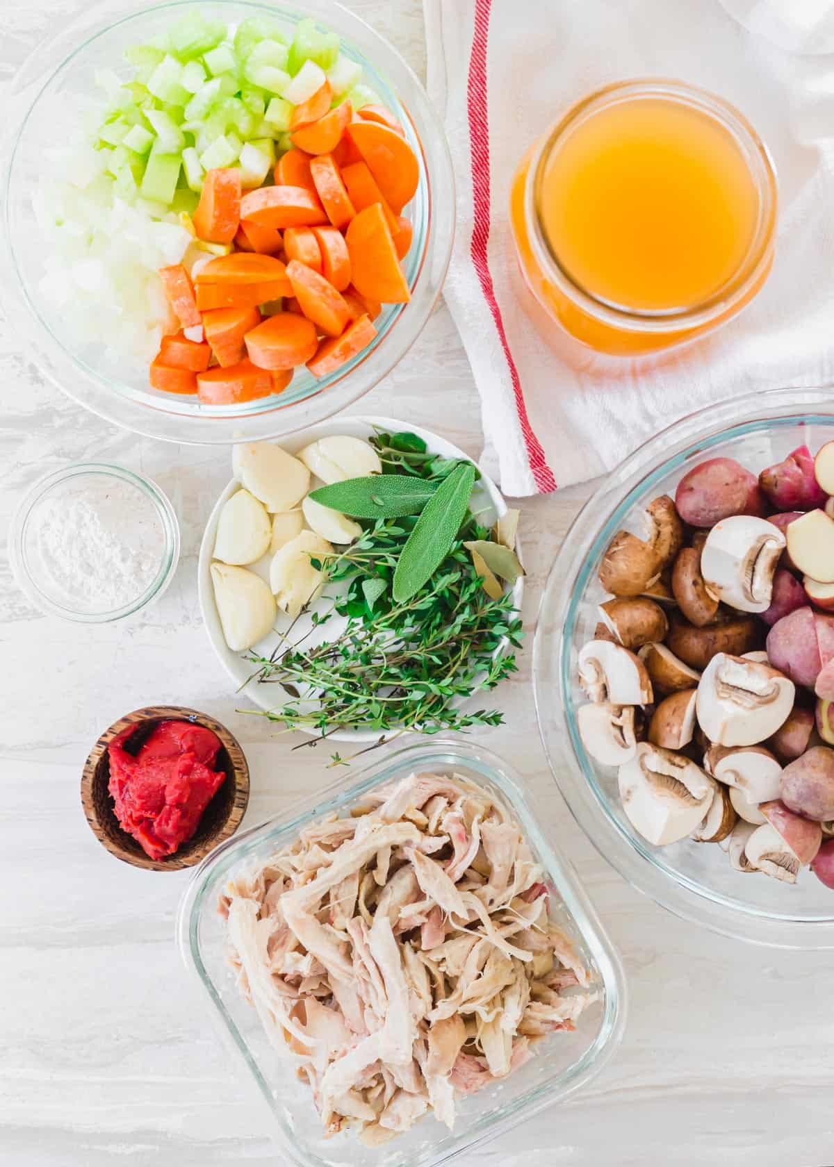 Ingredients to make turkey stew including red baby potatoes, mushrooms, tomato paste, garlic, fresh herbs, carrots, celery, onion, stock and shredded turkey.