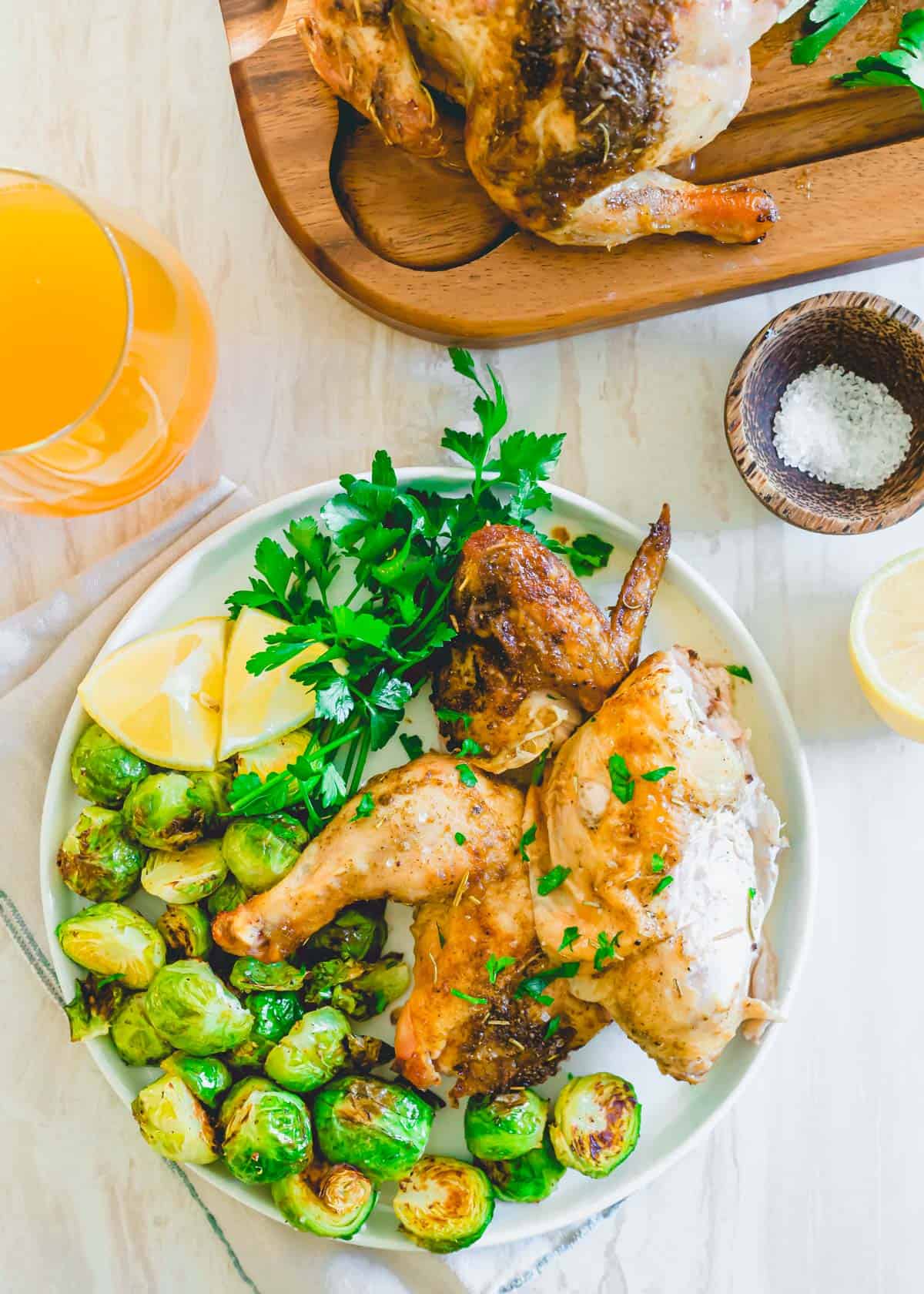 Tender juicy air fryer Cornish game hen cut into pieces on a plate with roasted Brussels sprouts.