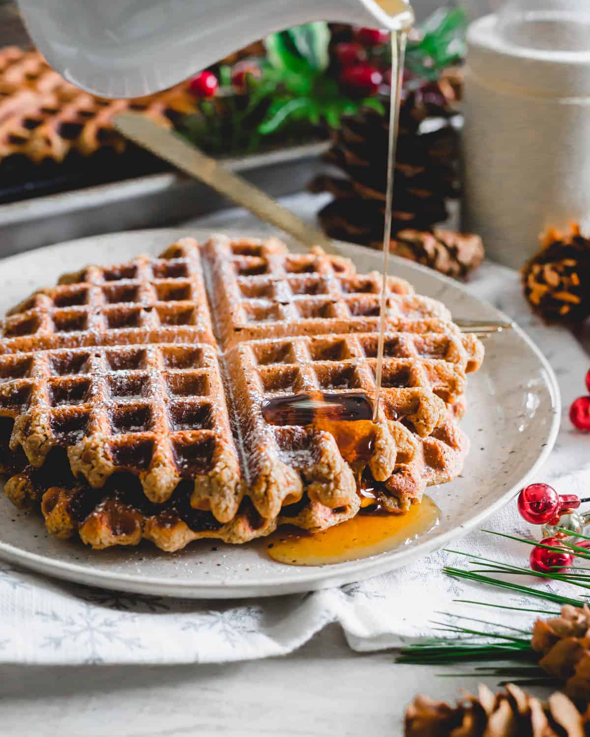 Pouring maple syrup on top of gingerbread waffles on a plate.