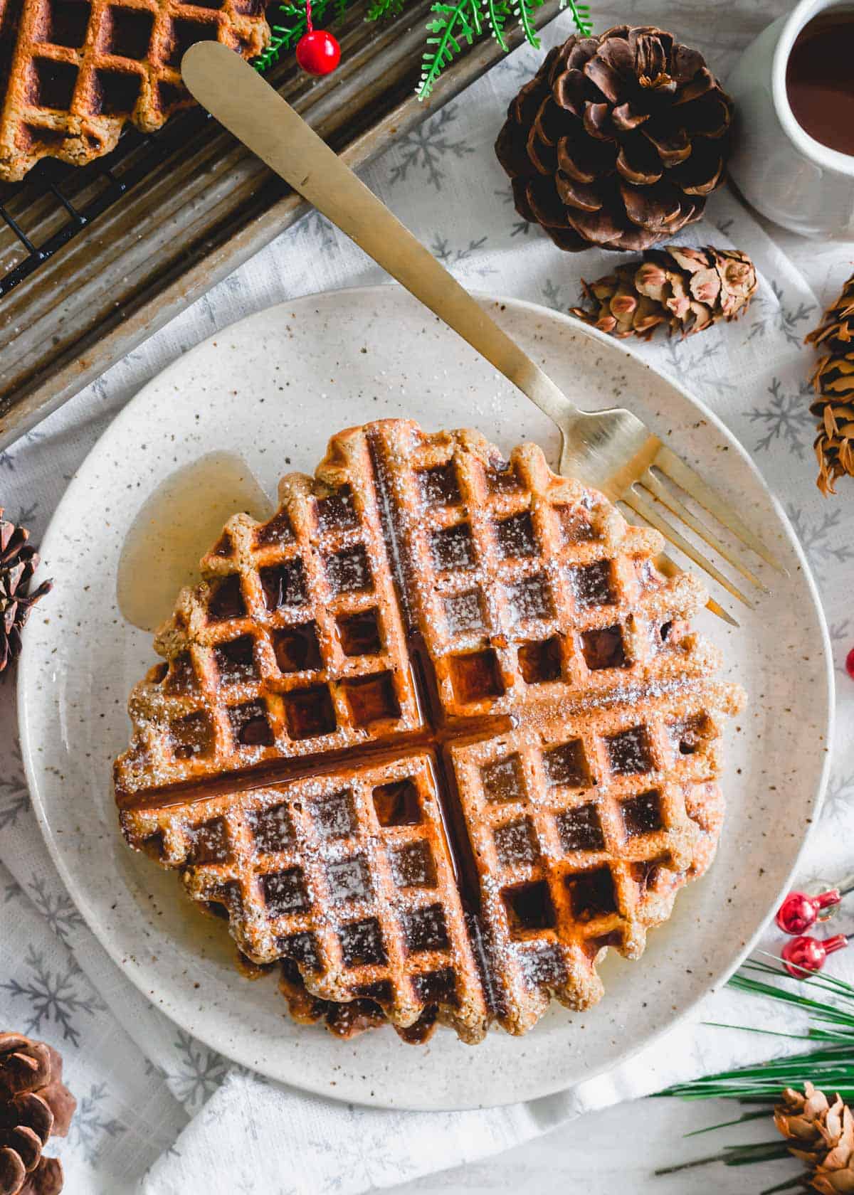 Cozy gingerbread waffles topped with powdered sugar and maple syrup on a plate.