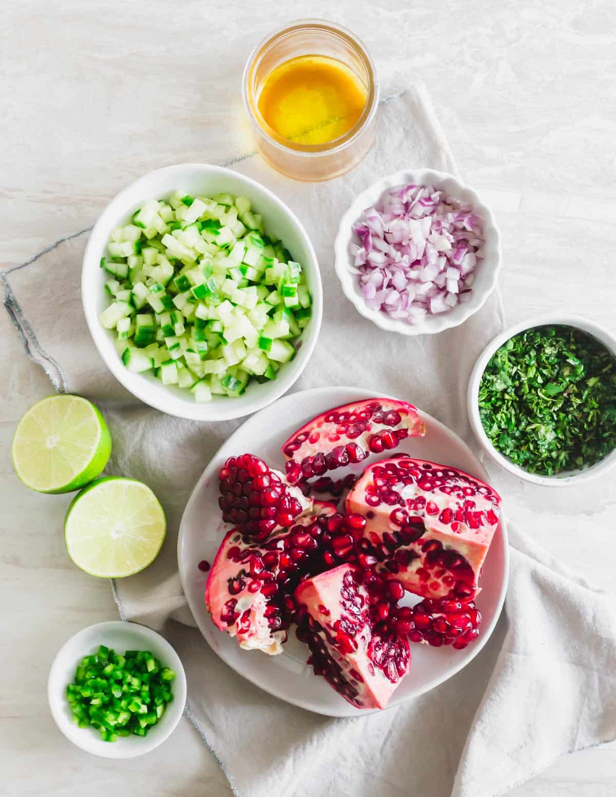 Ingredients to make pomegranate salsa including cucumber, red onion, lime, jalapeño, cilantro, mint and pomegranate arils.