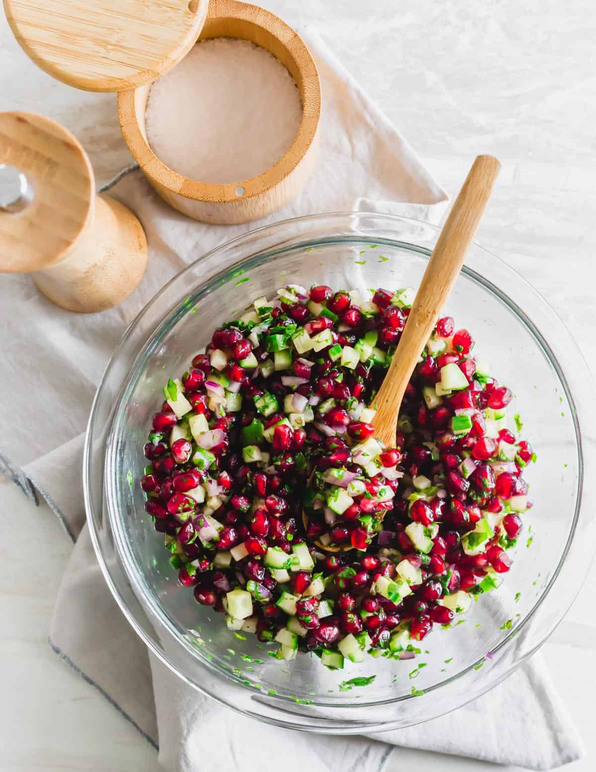 Mixing ingredients together to make pomegranate salsa in a glass bowl.