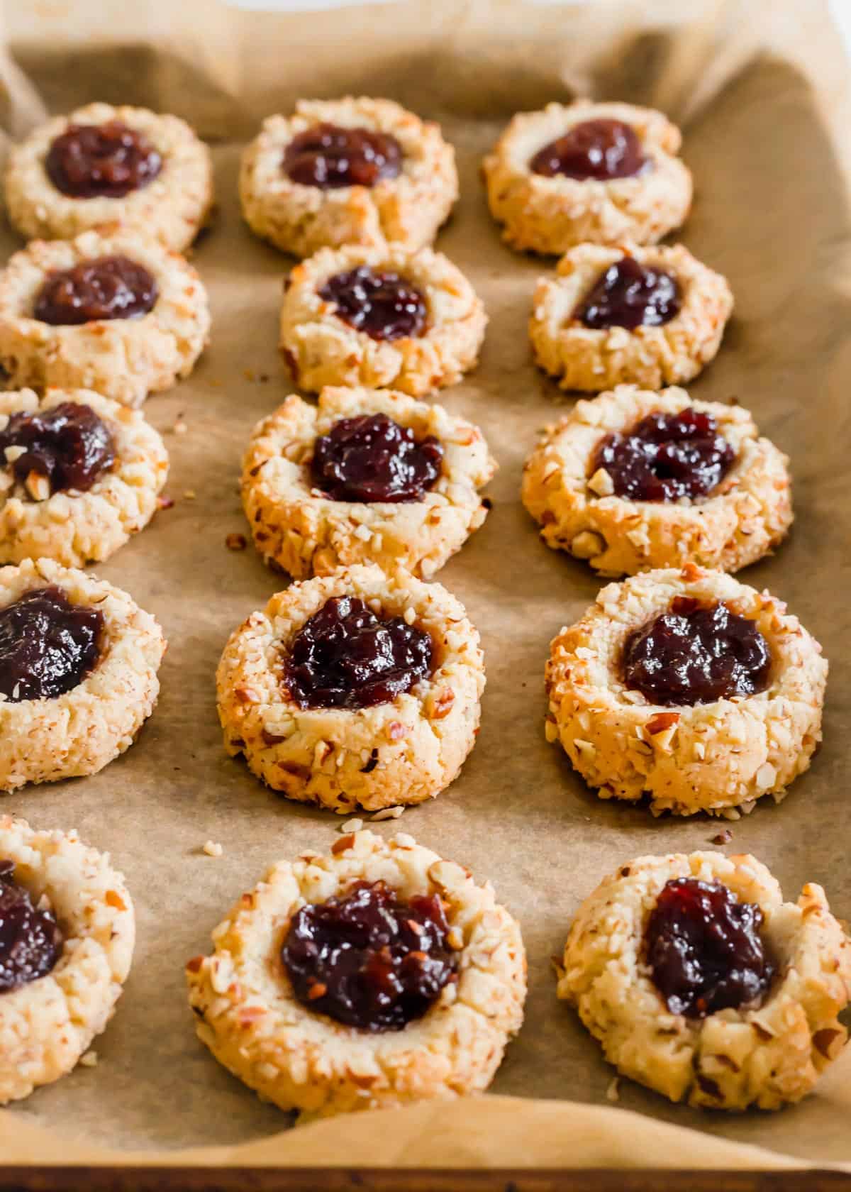 Baked almond flour thumbprint cookies with raspberry jam on a baking sheet.