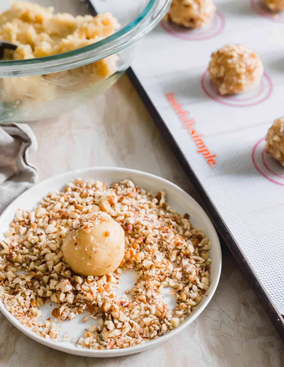 Rolling vegan thumbprint cookie dough balls in chopped pecans.