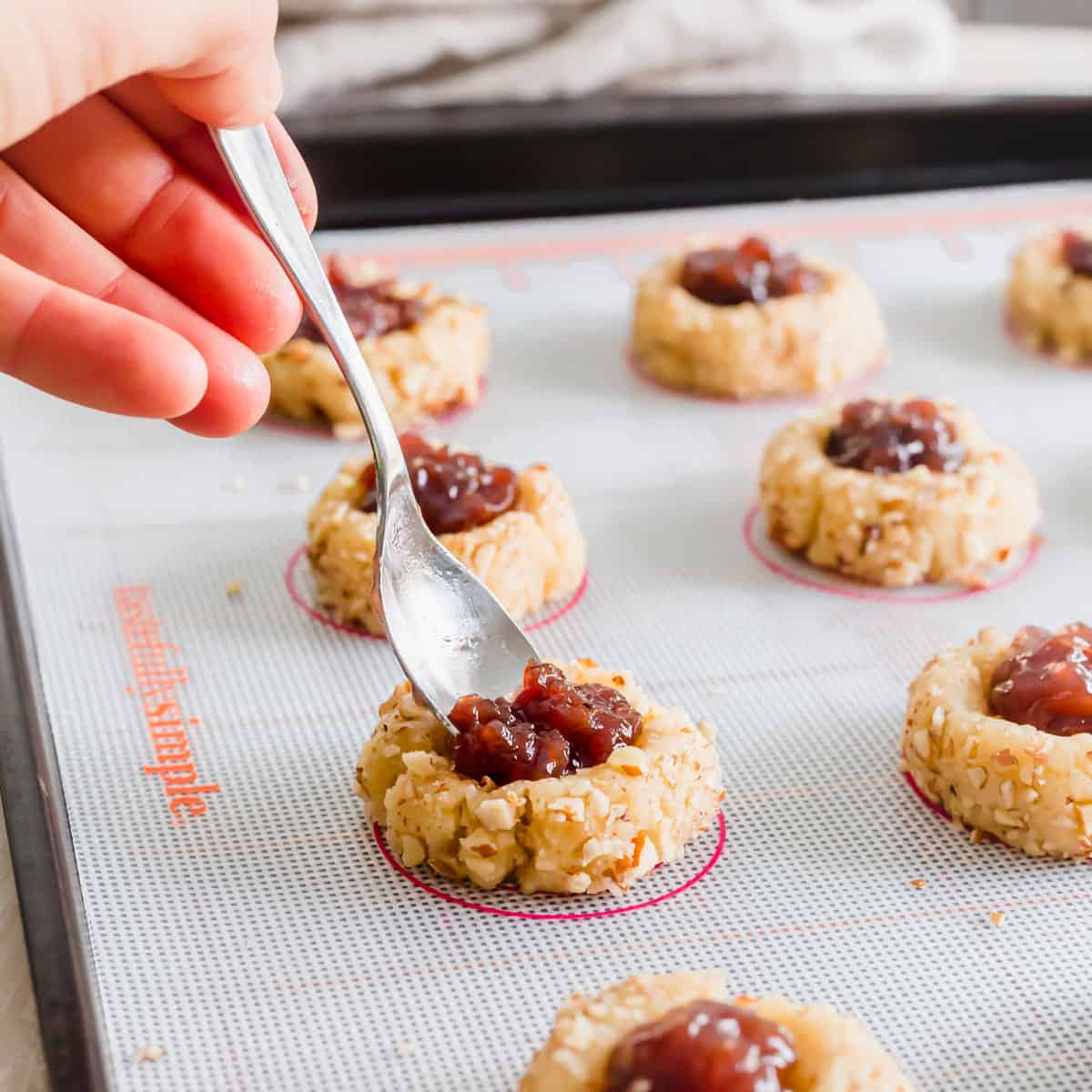 Filling vegan gluten-free thumbprint cookies with jam.