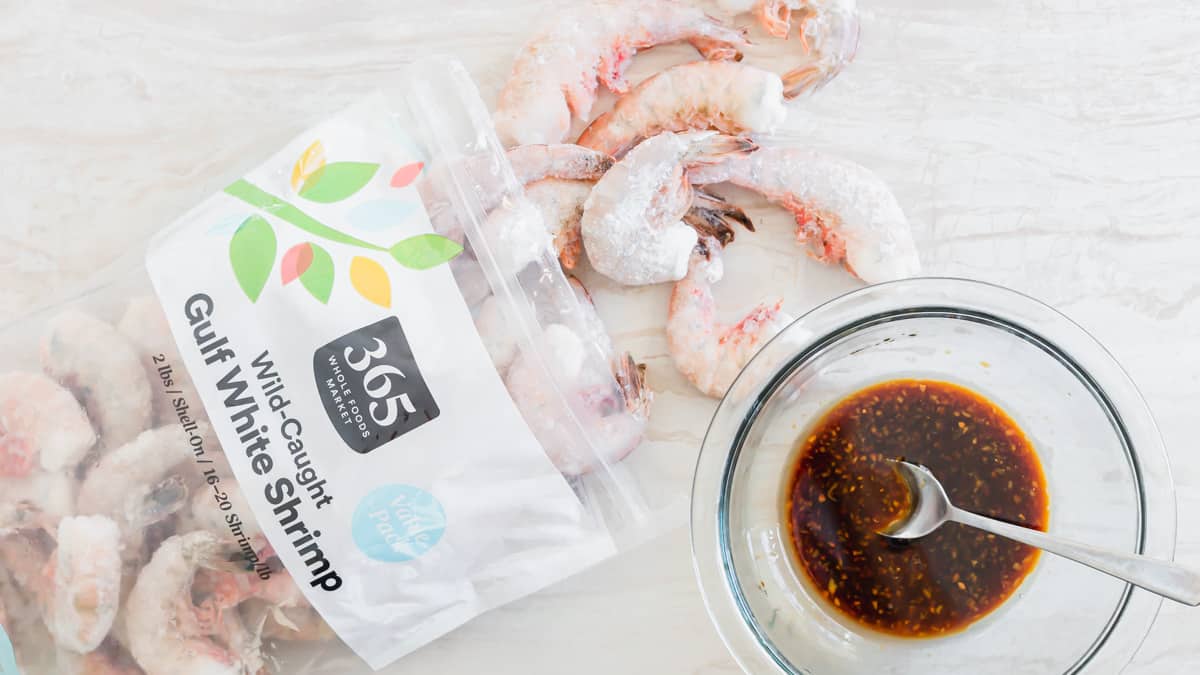 Bag of frozen wild-caught shrimp with a bowl of garlic, ginger, sesame marinade on the side.