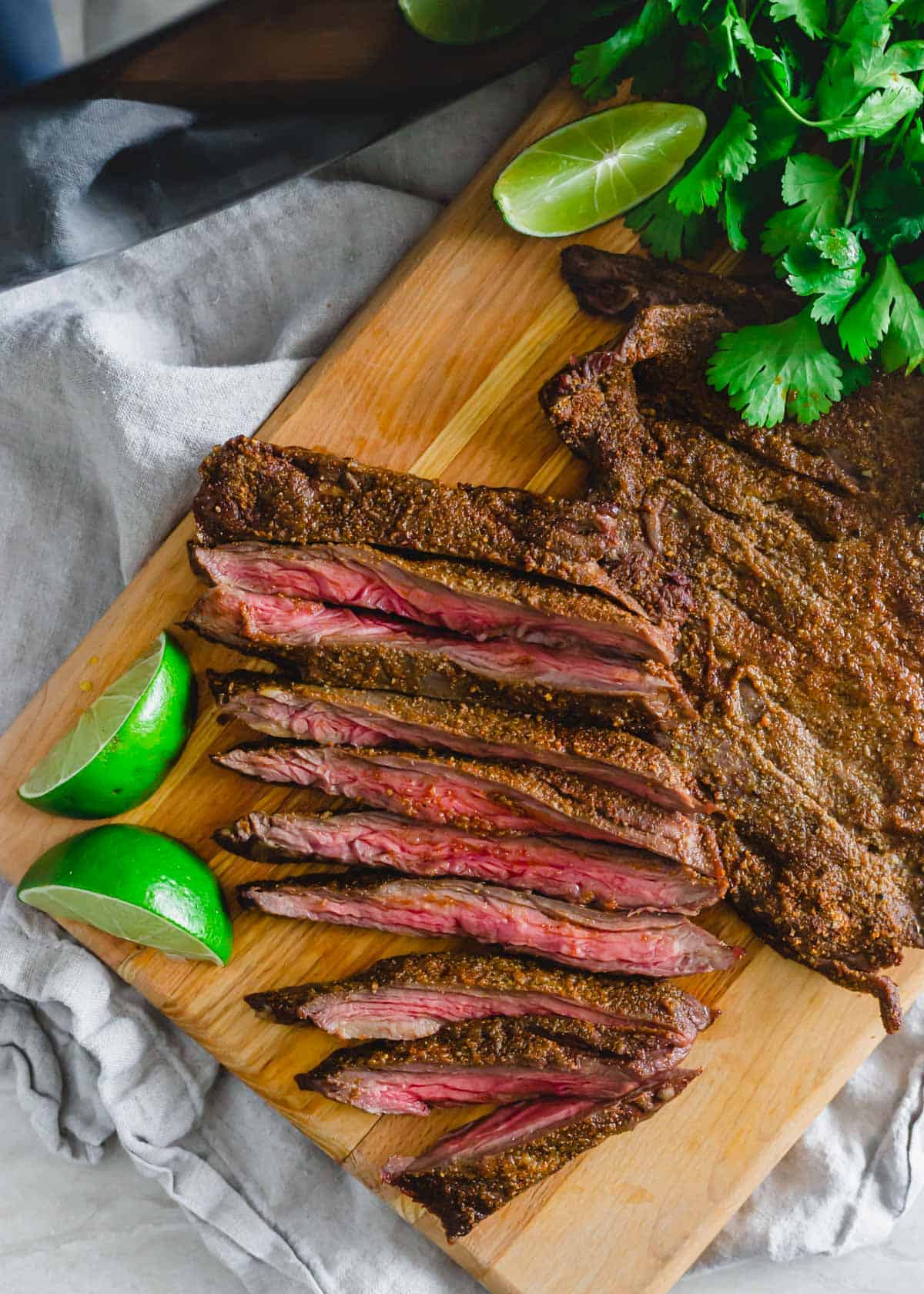 Air fryer skirt steak sliced on a cutting board with lime wedges and cilantro.