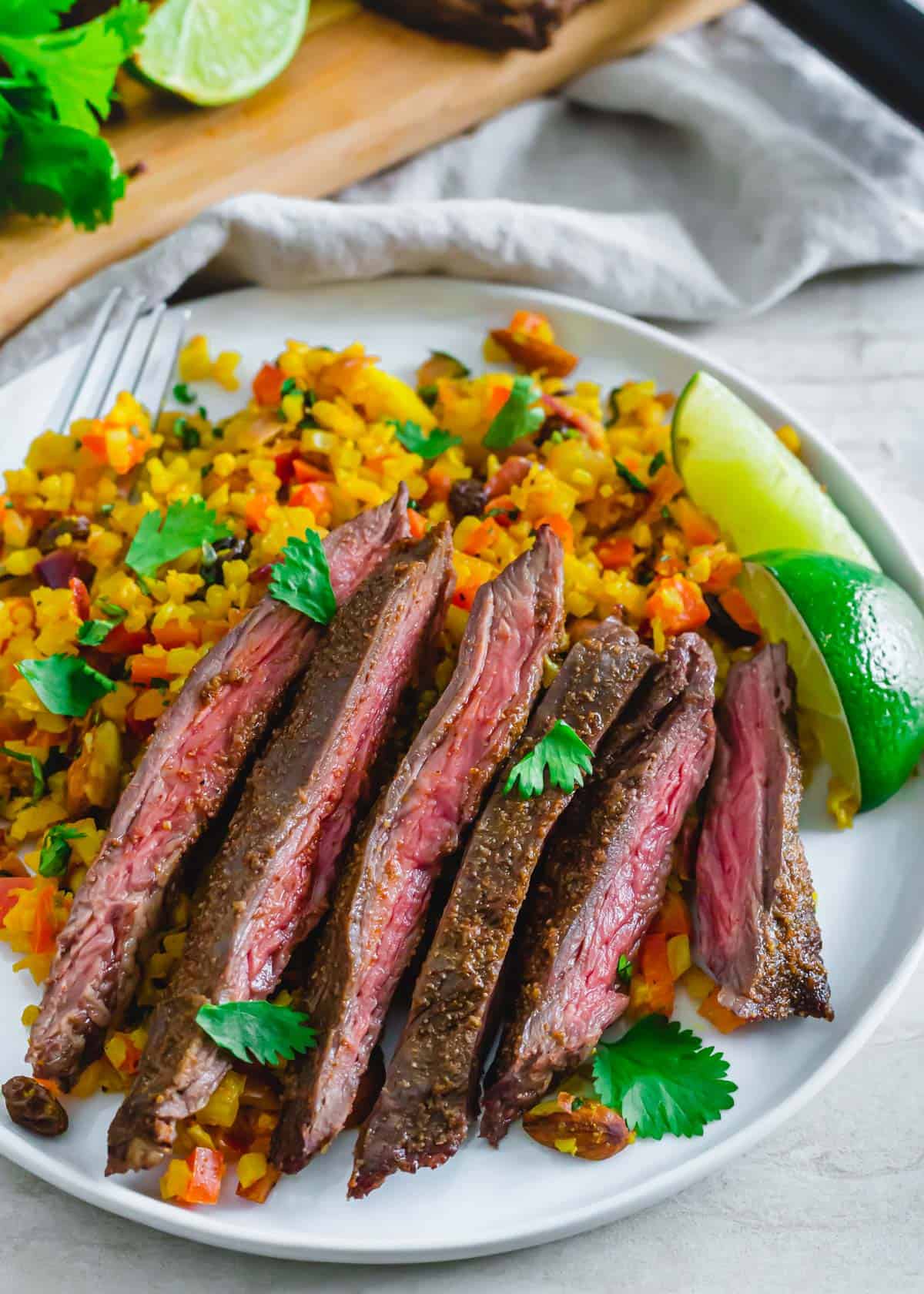 Carne asada seasoned skirt steak slices served over curry cauliflower rice on a white plate.