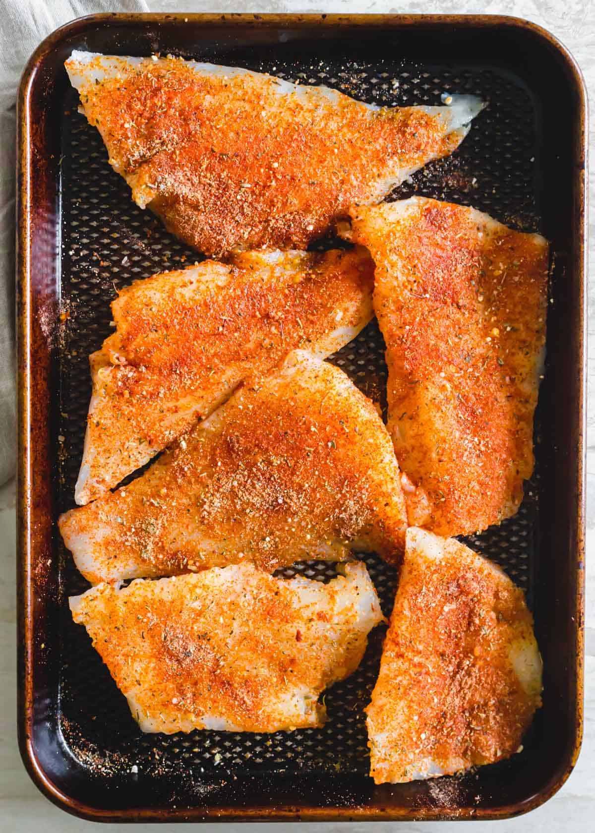 Cod filets on a baking sheet with blackening seasoning.