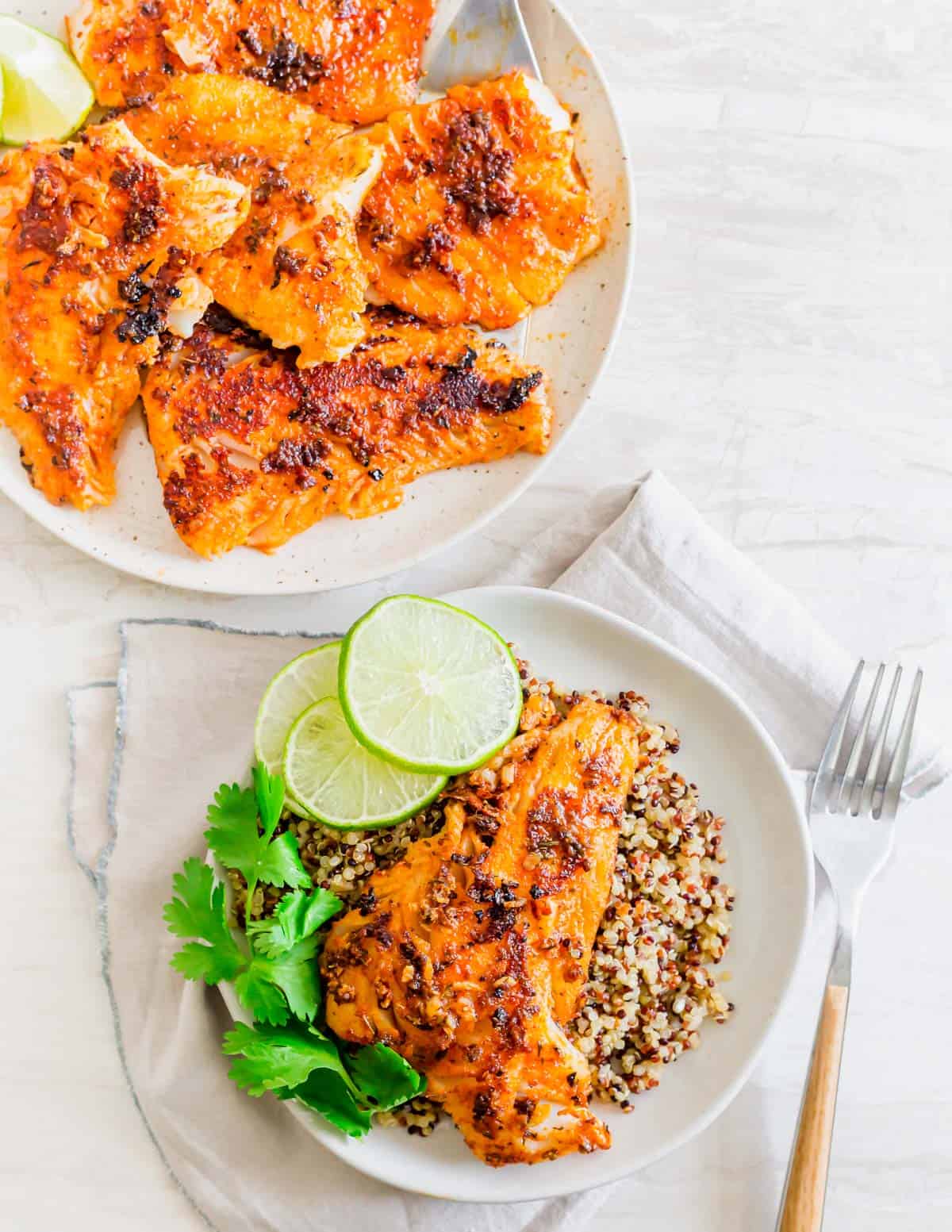 Cooked blackened cod on a plate in the background with a piece of blackened cod on a serving dish with quinoa, lime and cilantro.