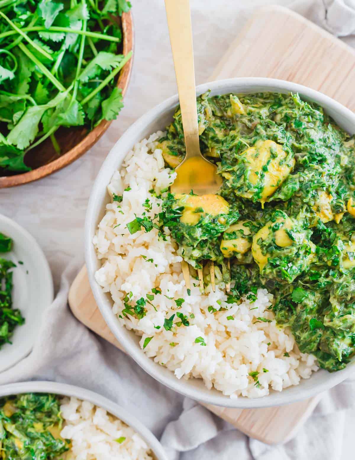 Dairy free chicken saag recipe in a bowl with basmati rice, fresh mint and cilantro and a serving fork.