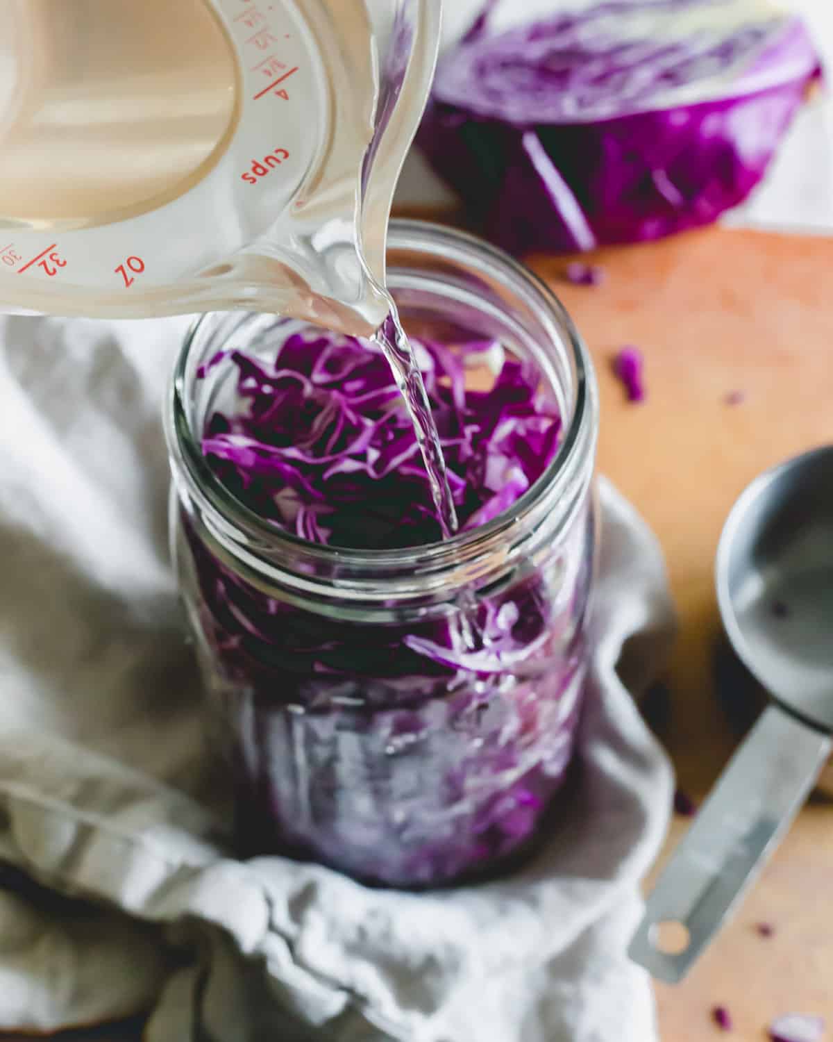 Pouring brine over red cabbage in a mason jar to make sauerkraut.