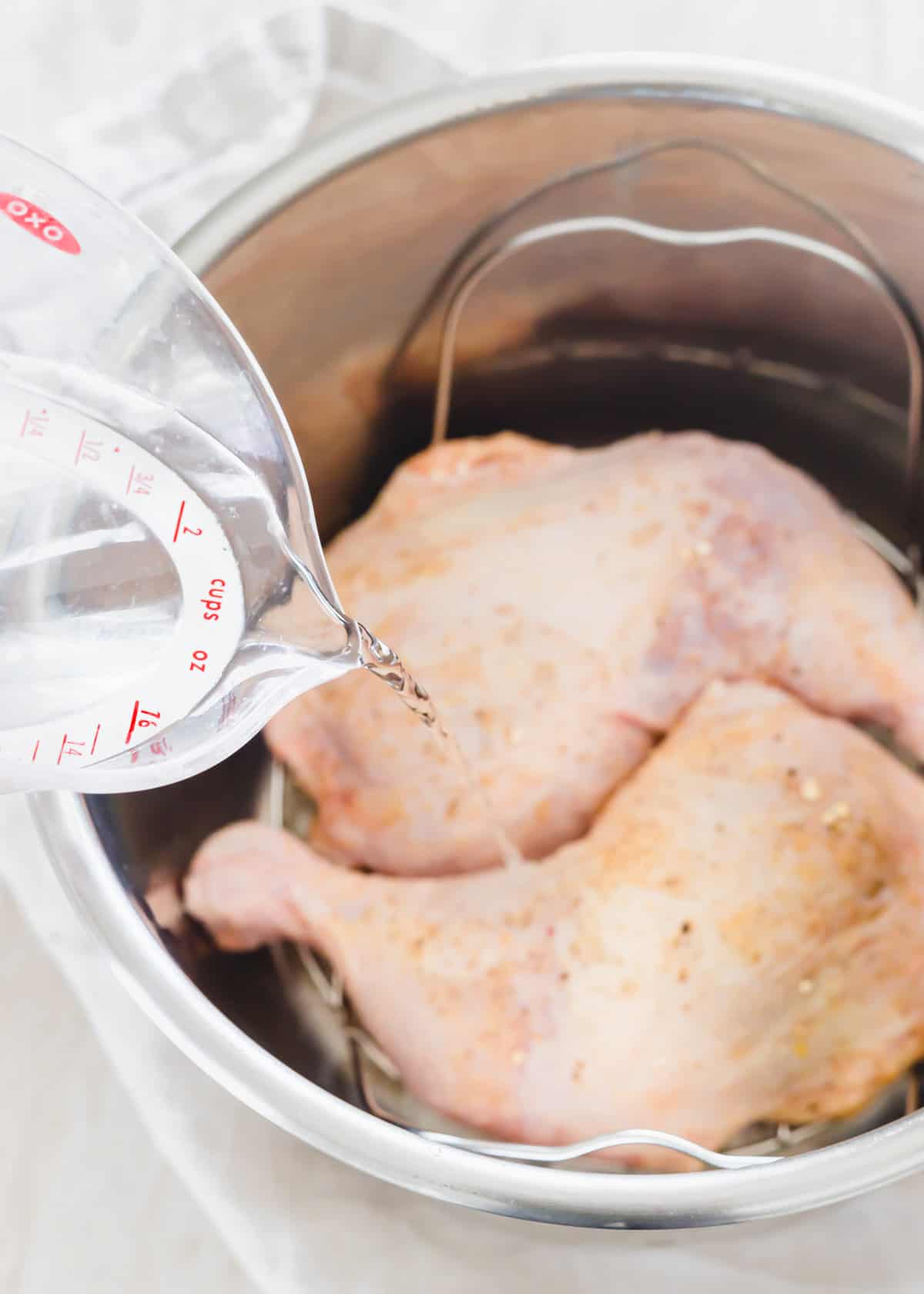 Pouring water into the Instant Pot with seasoned chicken leg quarters on the trivet.