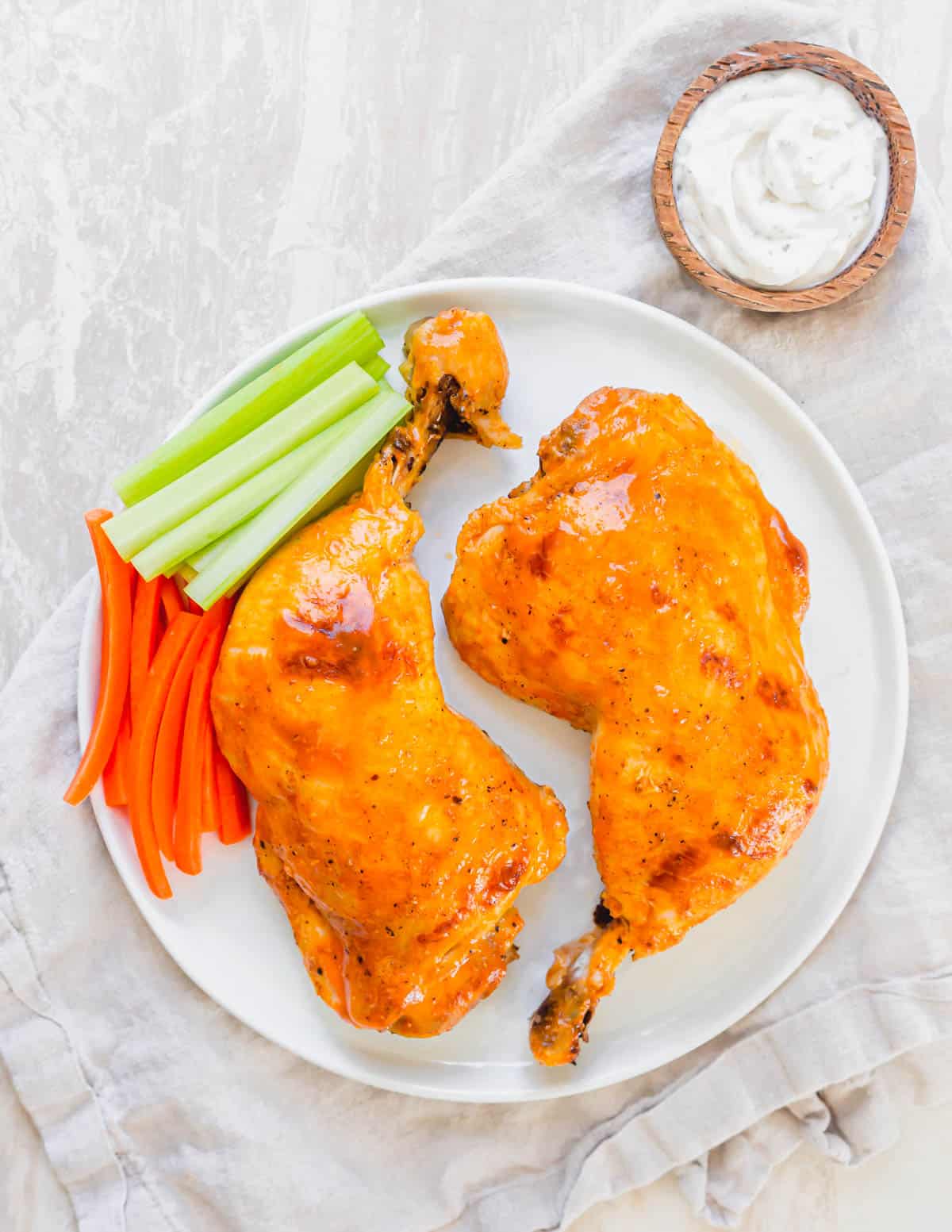 Overhead picture of two buffalo sauce chicken leg quarters cooked in the Instant Pot on a white plate with celery and carrots.