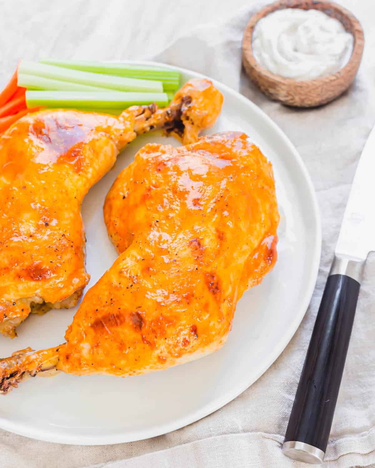 Close up picture of one buffalo chicken leg quarter on a plate with dipping sauce in the background.