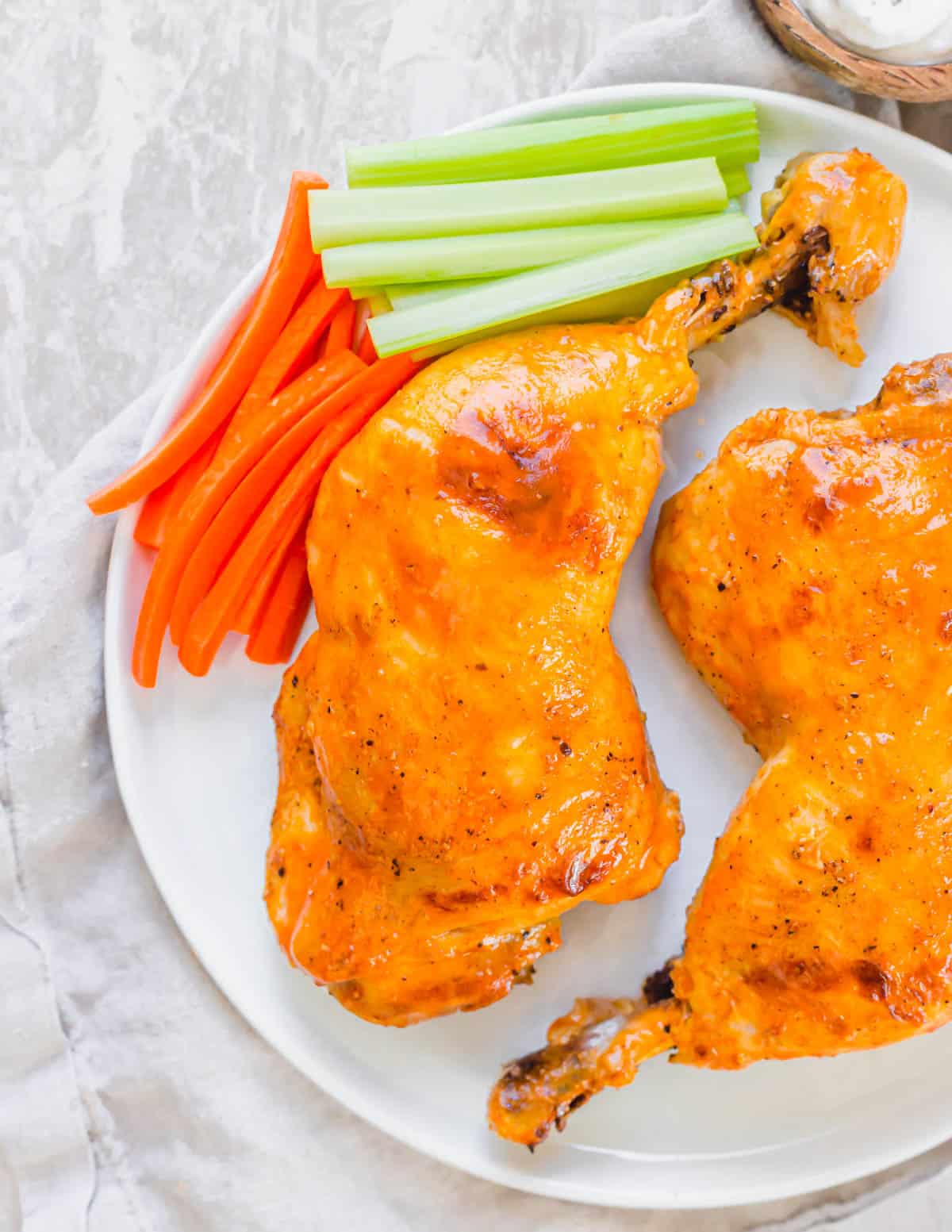 Instant Pot chicken leg quarters brushed with buffalo sauce on a white plate with carrots and celery sticks.