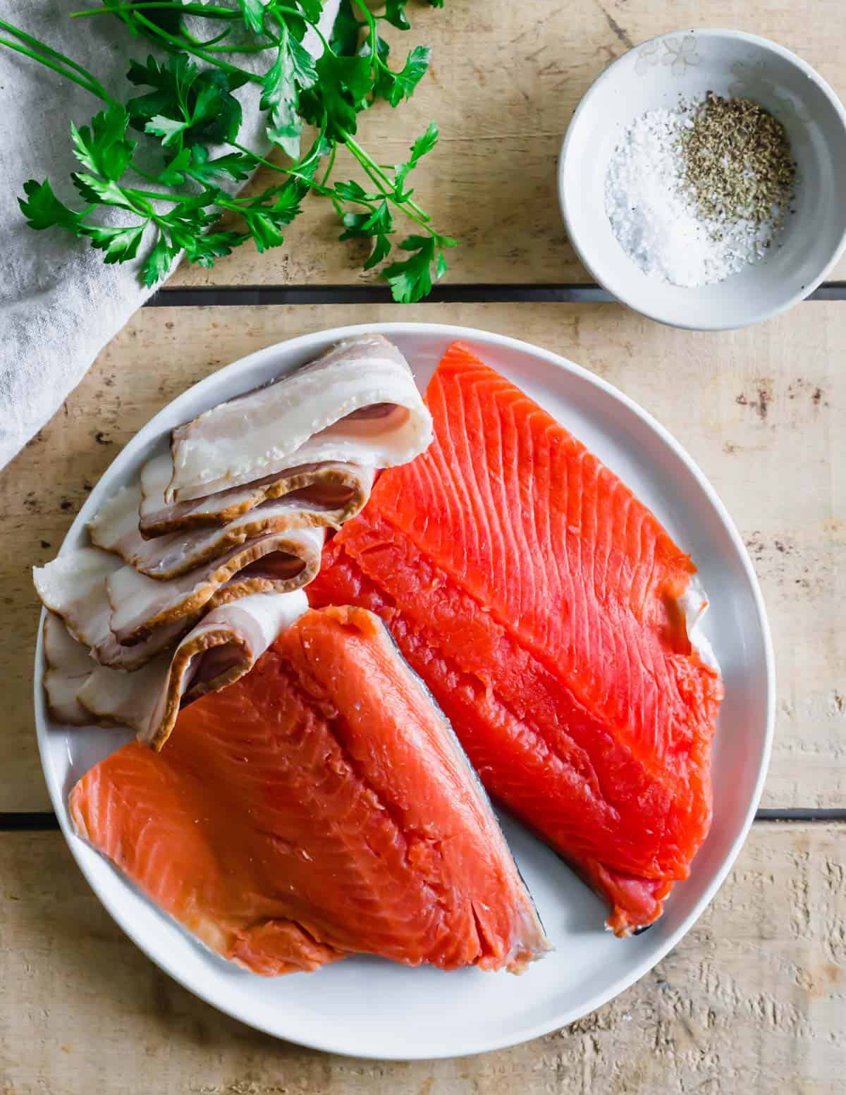 Uncooked wild salmon filets on a plate with slices of bacon.