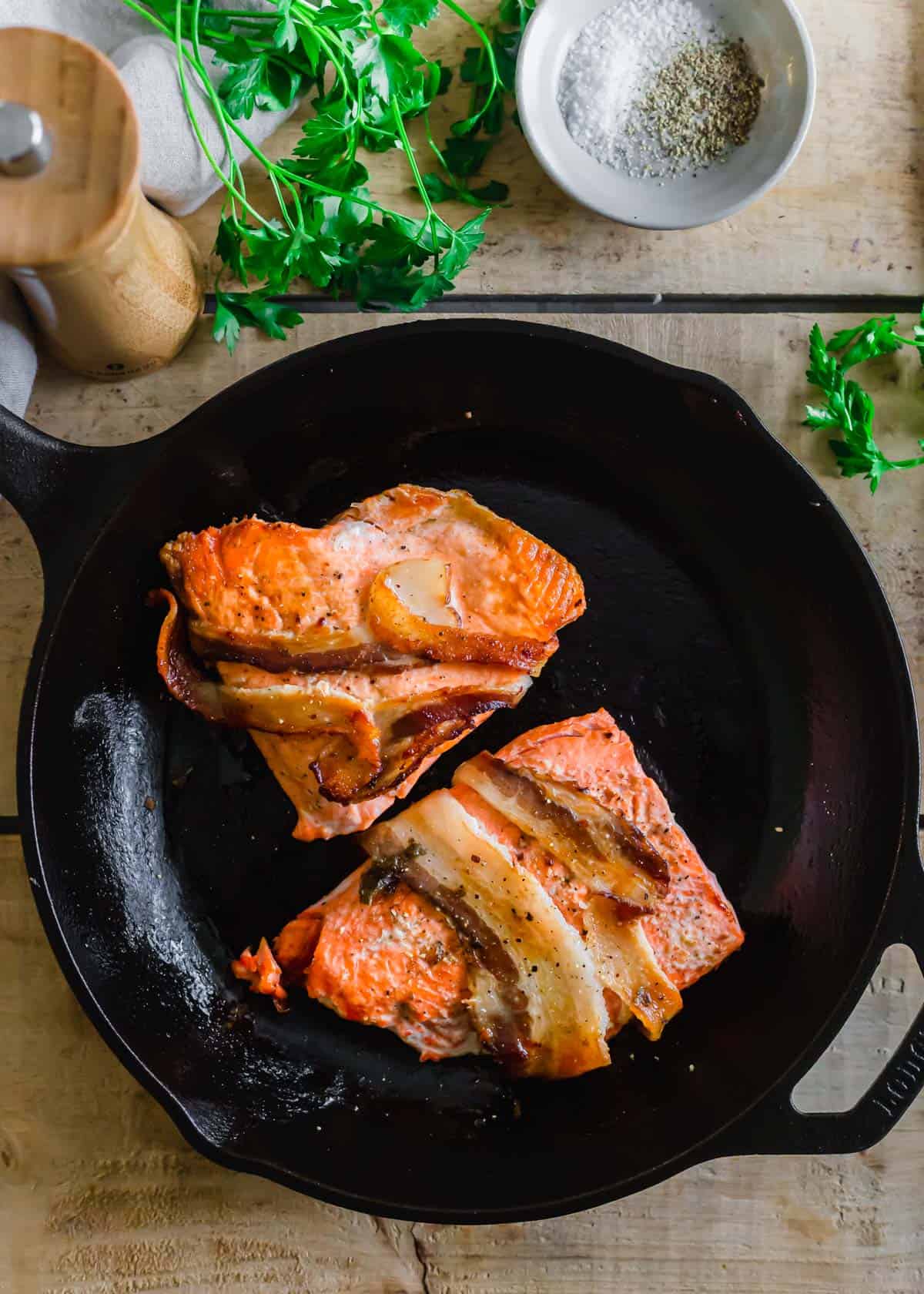 Pan-seared salmon wrapped in bacon in cast iron skillet.
