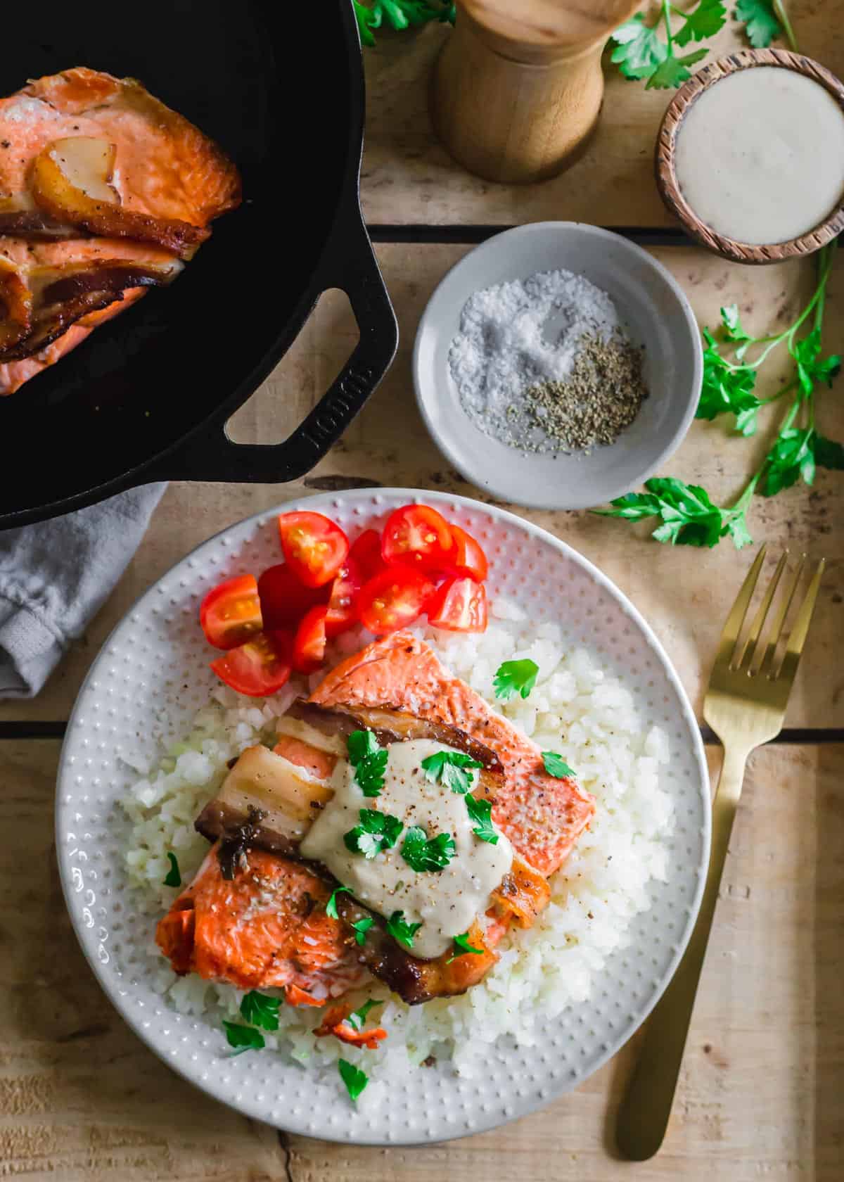 Bacon-wrapped salmon recipe on a plate with sliced cherry tomatoes and cauliflower rice.