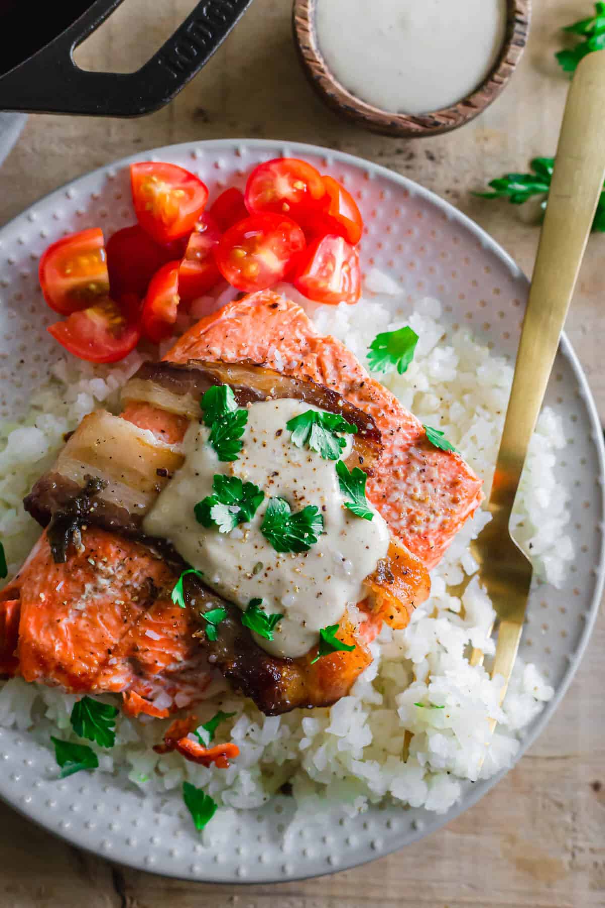 Bacon wrapped salmon with creamy tahini sauce on top of cauliflower rice on a plate.