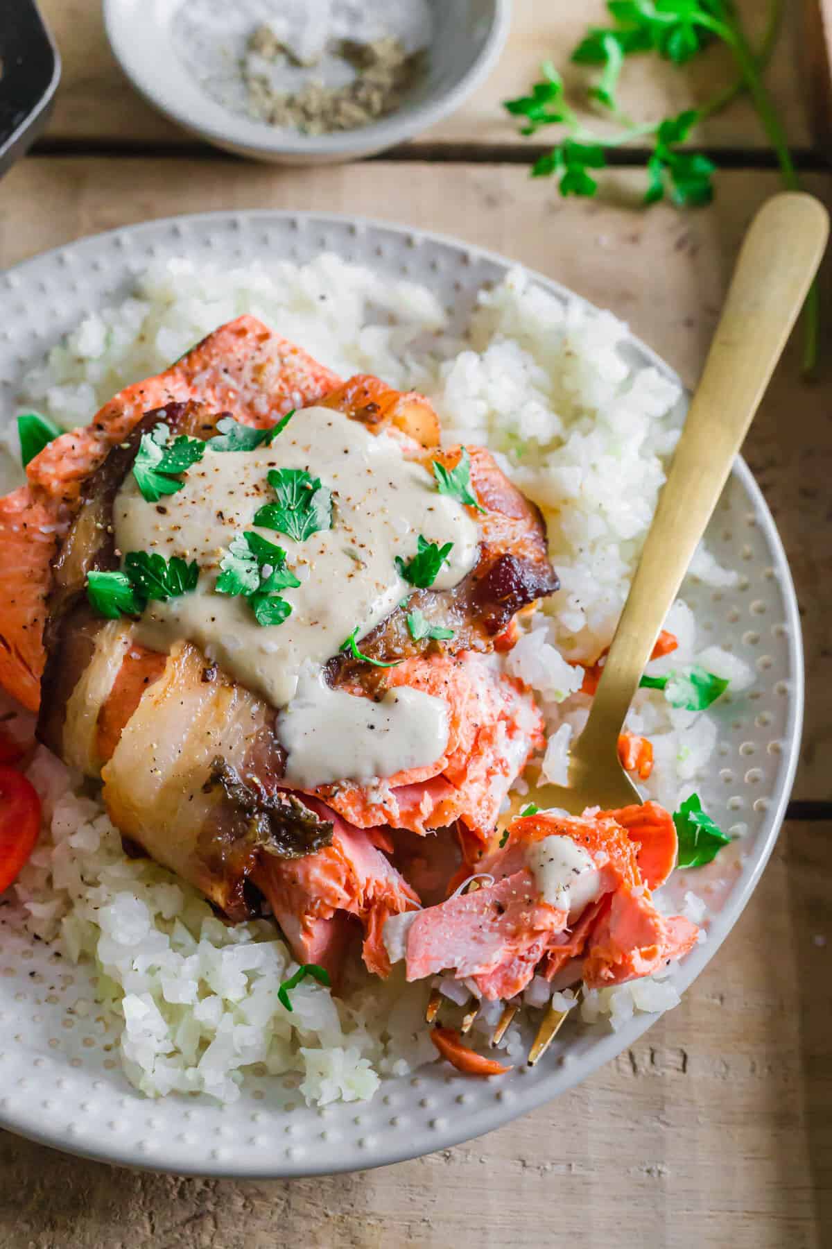 Cooked wild salmon wrapped in bacon on a plate with a fork.