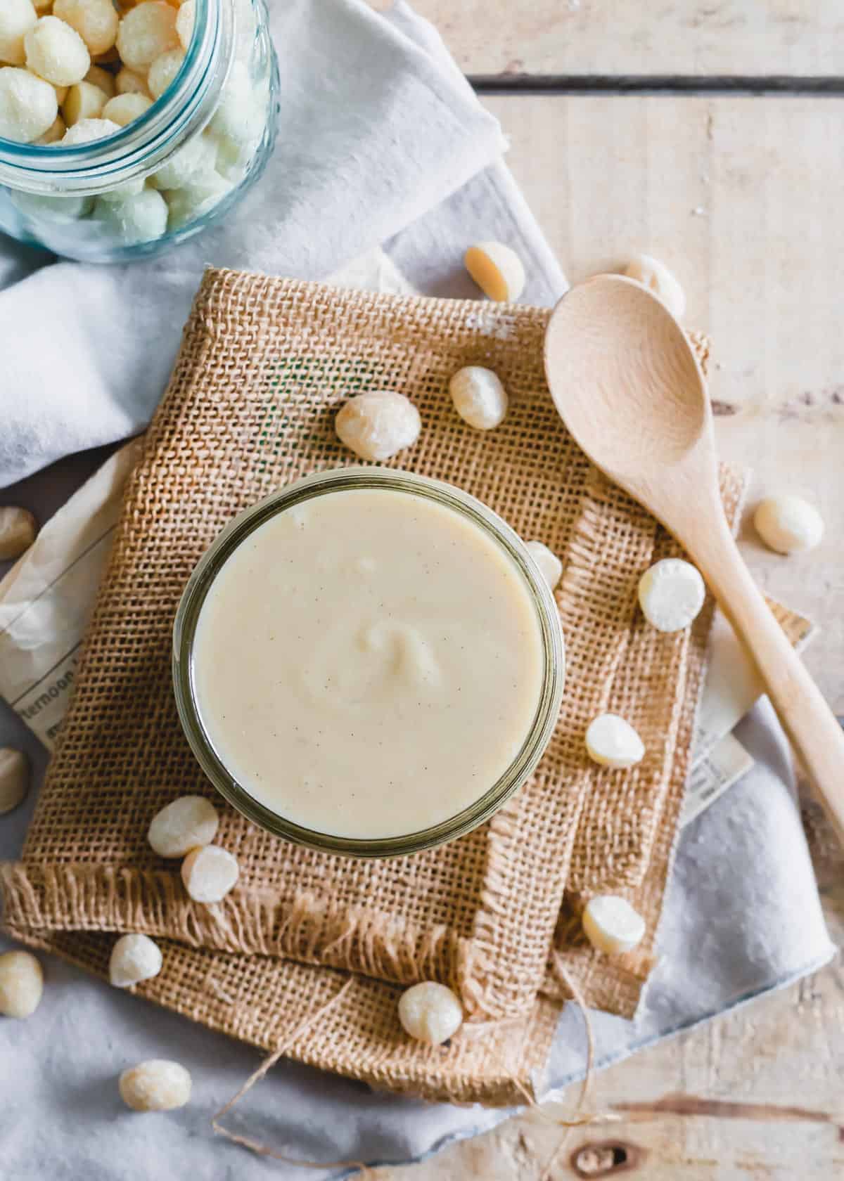 Creamy homemade macadamia nut butter in a jar with a wooden spoon on the side.