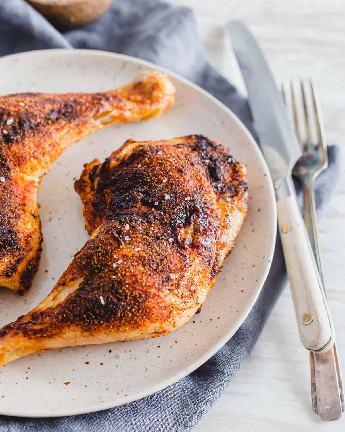 Crispy air fried chicken leg quarters with spice rub and coarse salt on a plate.