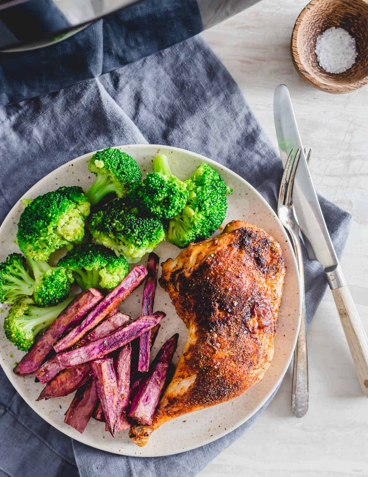 Chicken leg quarters roasted in the air fryer on a plate with broccoli and sweet potato fries.