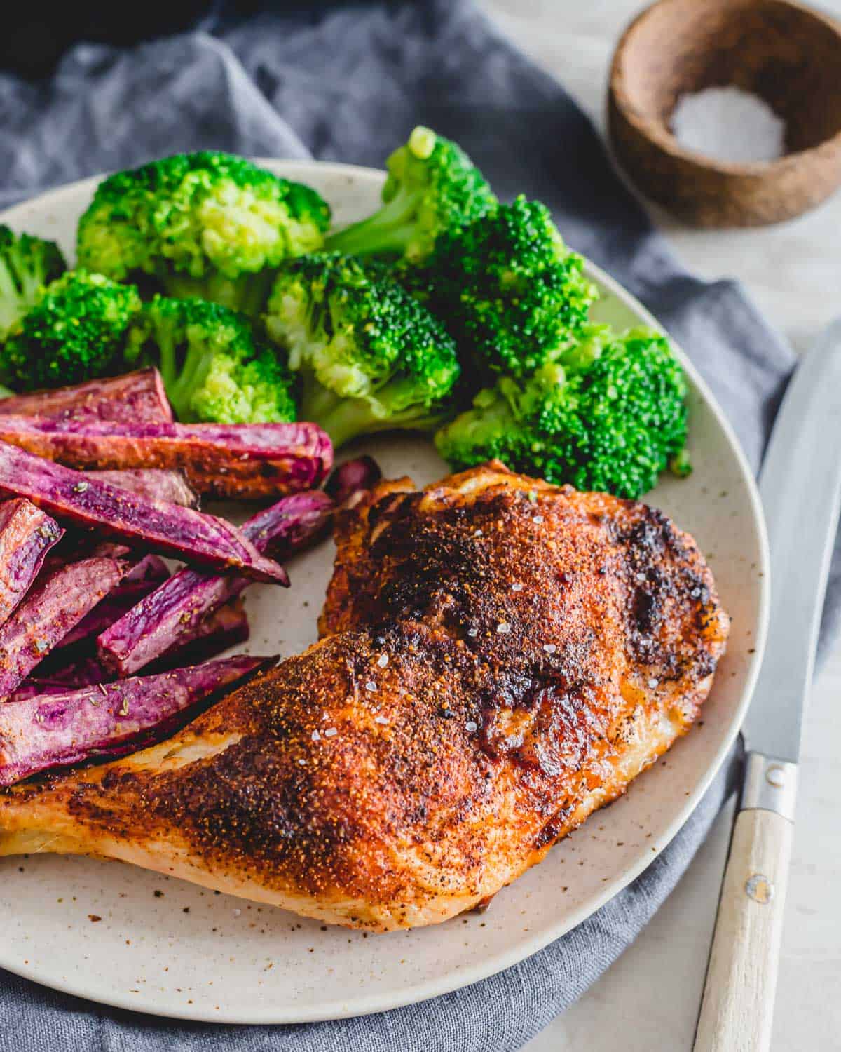 Spice rubbed air fryer chicken leg quarters on a plate with broccoli and purple sweet potato fries.