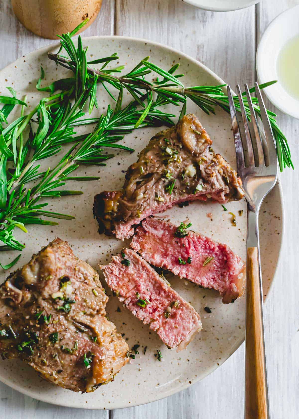 Medium-rare cooked lamb chop made in the air fryer on a plate with fresh rosemary.