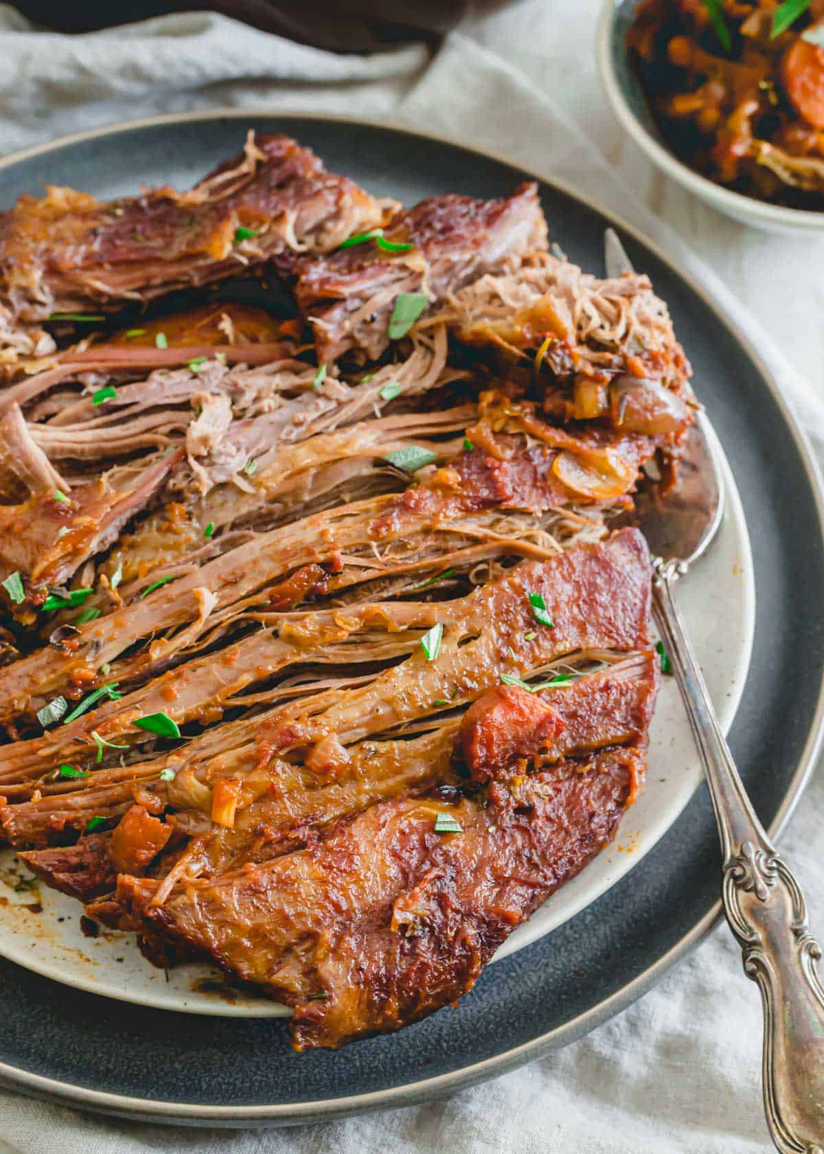 Sliced veal brisket with fresh herb garnish on a plate with a fork.